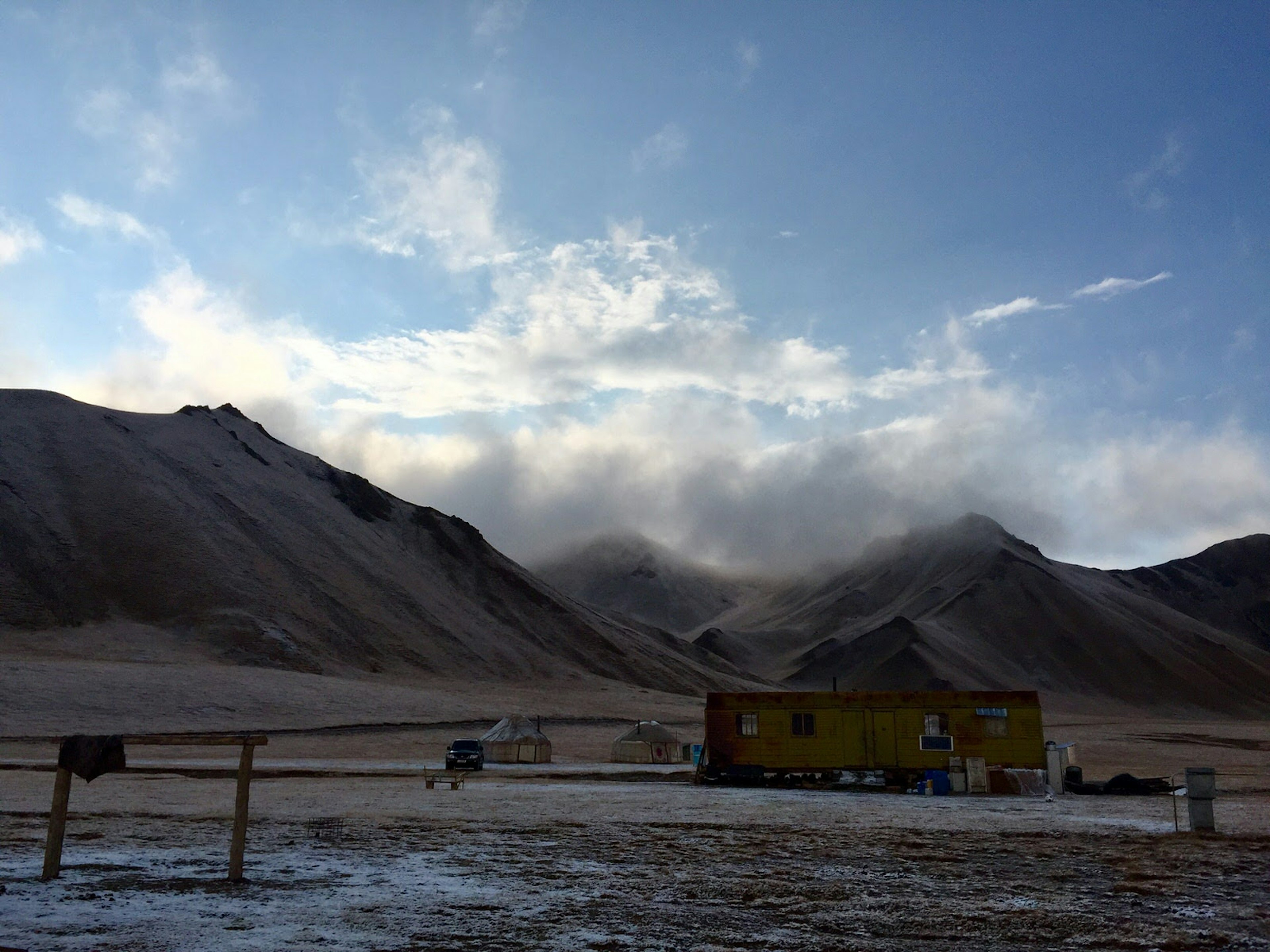 A yellow wagon and hitching post in front of several white yurts, with mountains and fog in the distance © Megan Eaves / Lonely Planet