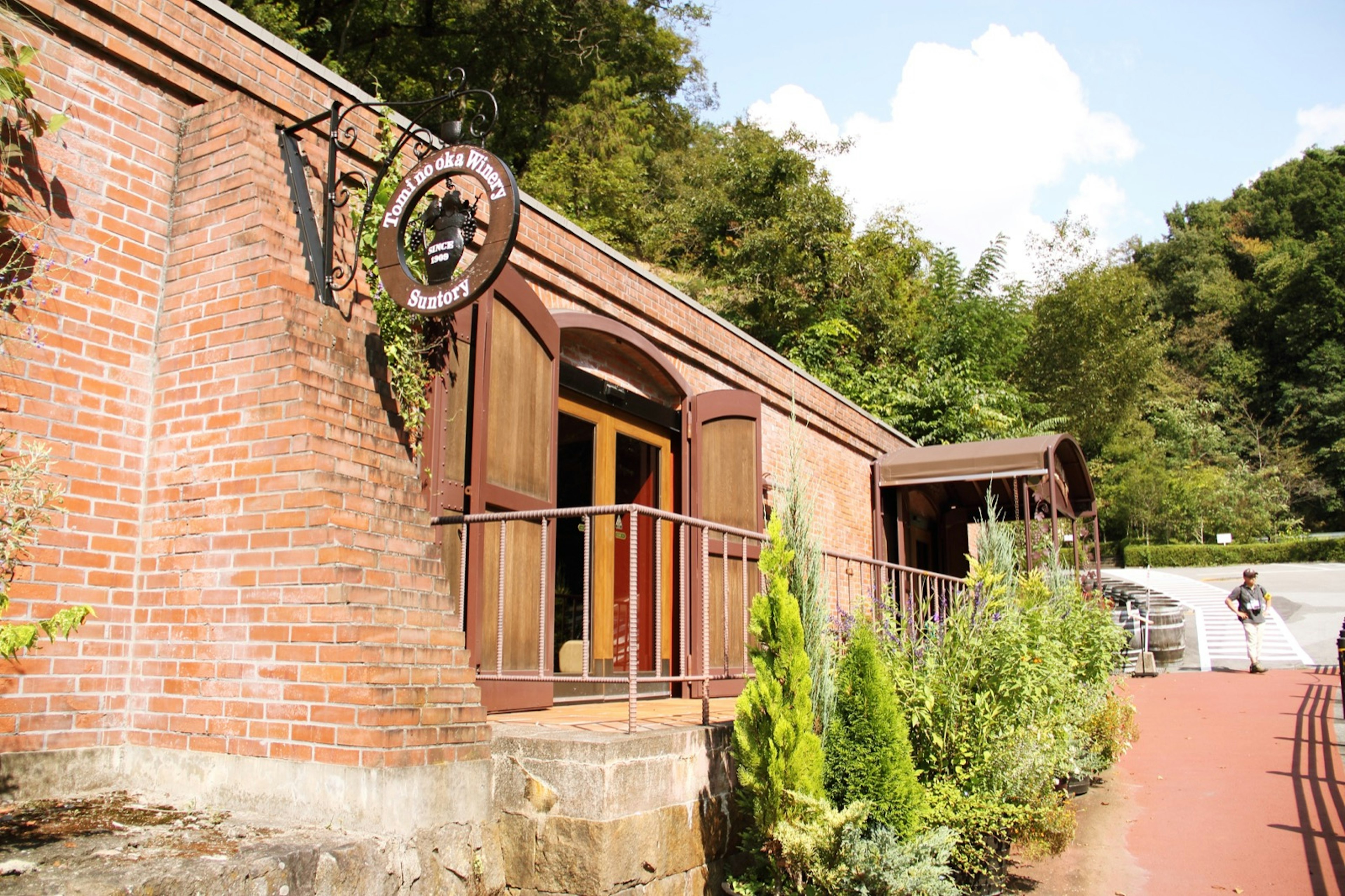 The brick facade of a cozy winery in Yamanashi Prefecture, Japan, features a round nameplate featuring an urn full of grapes and the label 'since 1909.'