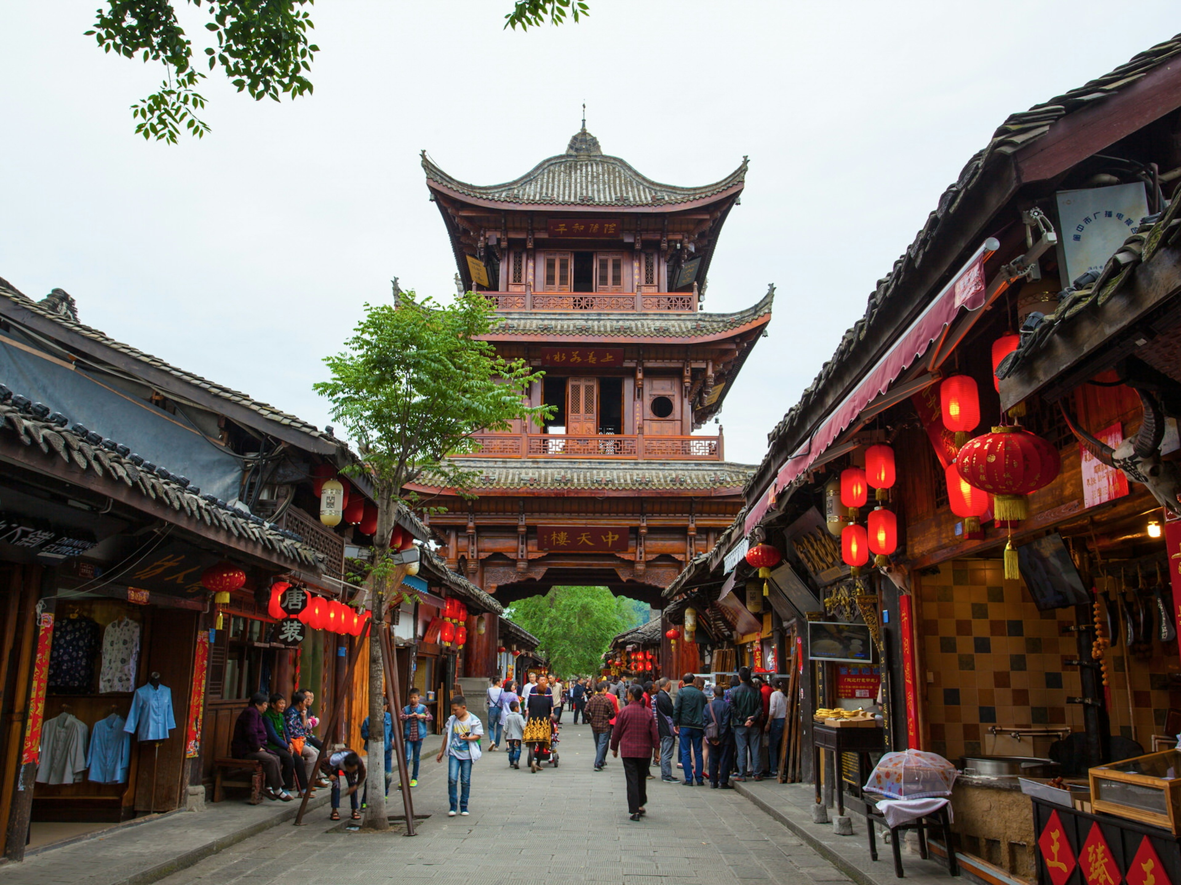 A historic Chinese street lined by red lanterns with a multi-storey traditional gate with upturned eaves. Historic, chilled-out Langzhong is a good place to discover ancient Chinese culture and literature ? Meiqianbao / Shutterstock