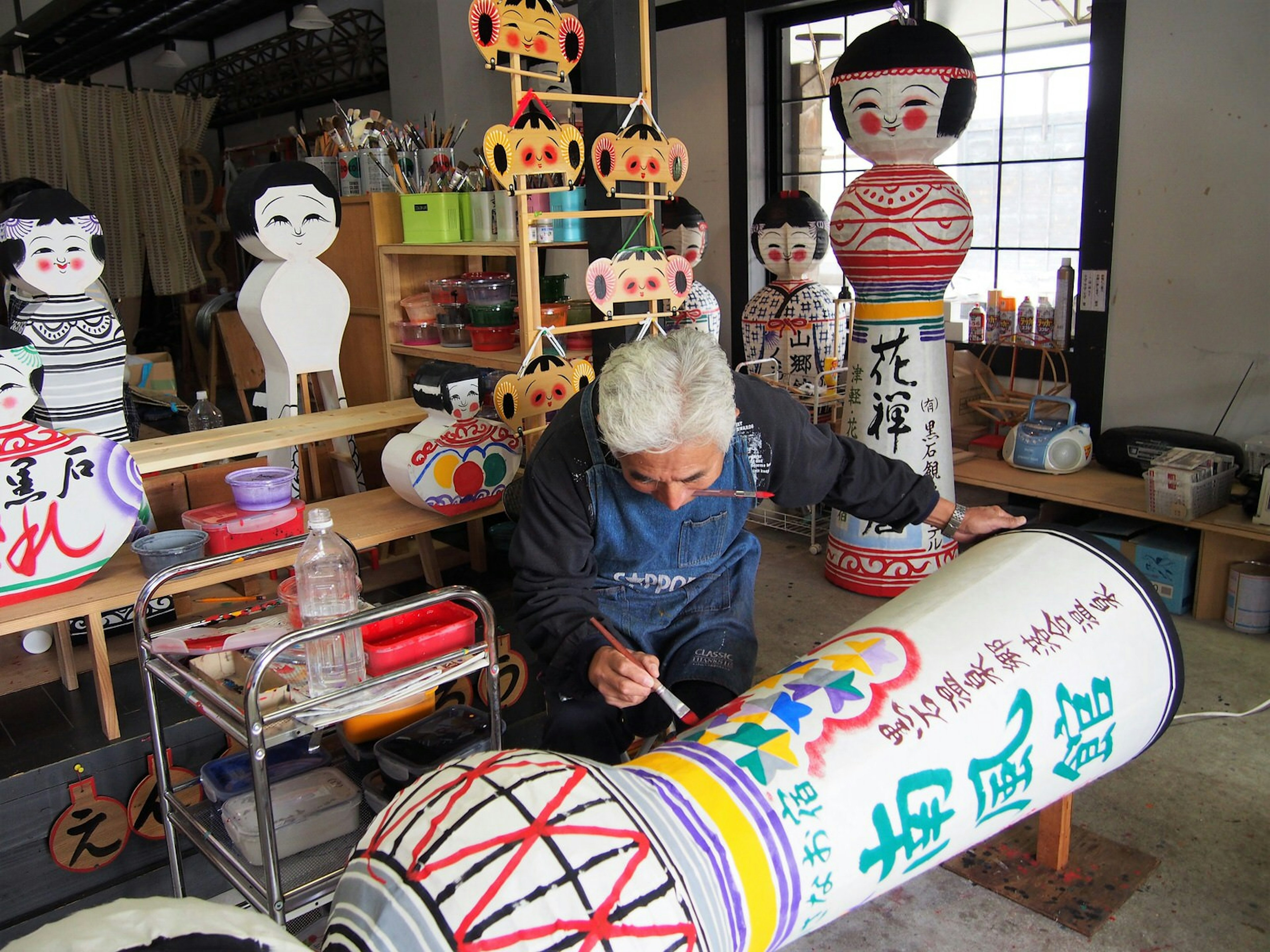 Artisan Yuichi Mori painting motifs onto a large paper lantern in his studio, surrounding by other lanterns © Manami Okazaki / Lonely Planet