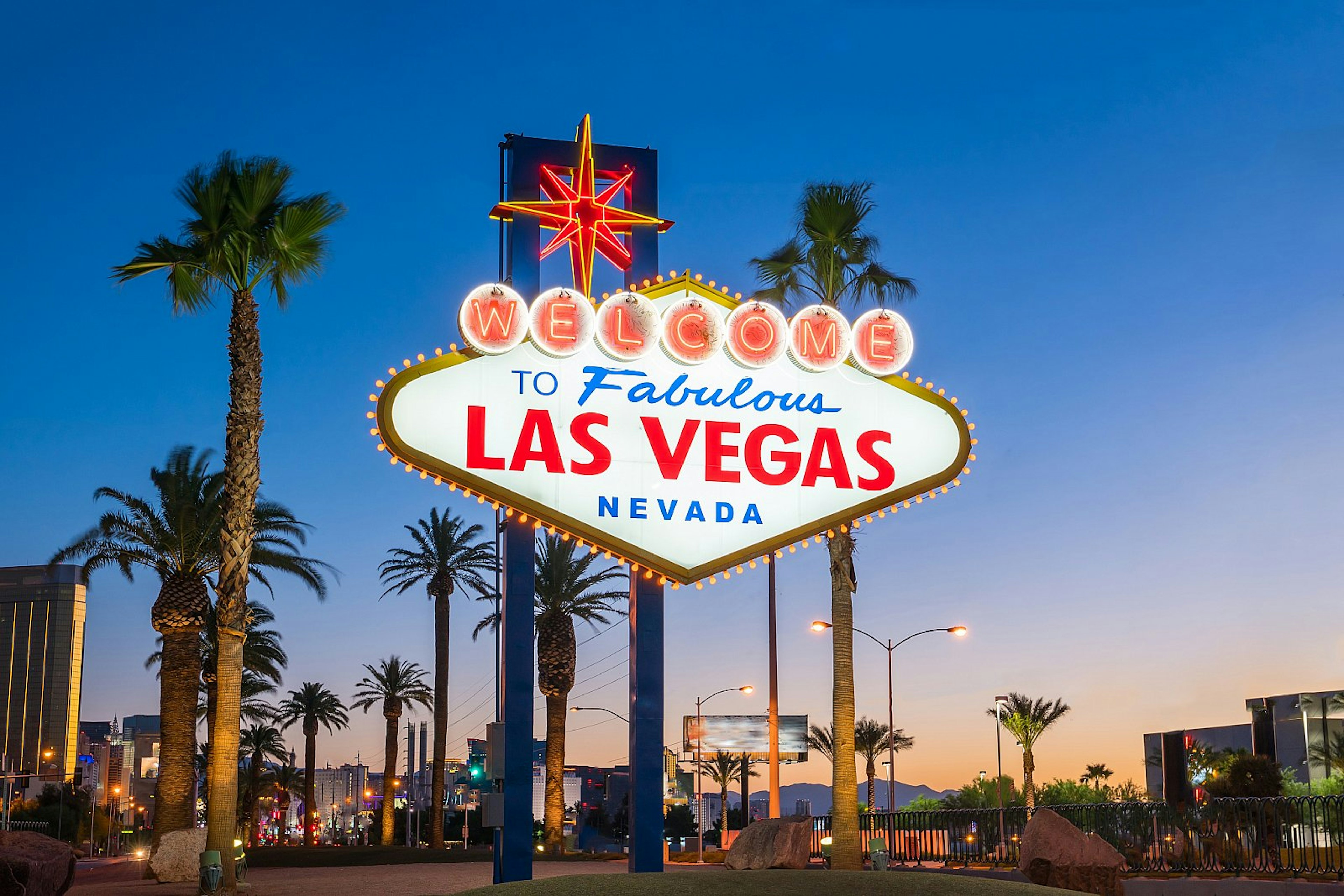 The huge, lit-up Welcome to Fabulous Las Vegas sign in Las Vegas, Nevada at dusk, with palm trees beyond.