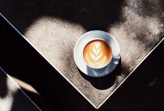 A latte sits on a concrete table in a spot of sunshine