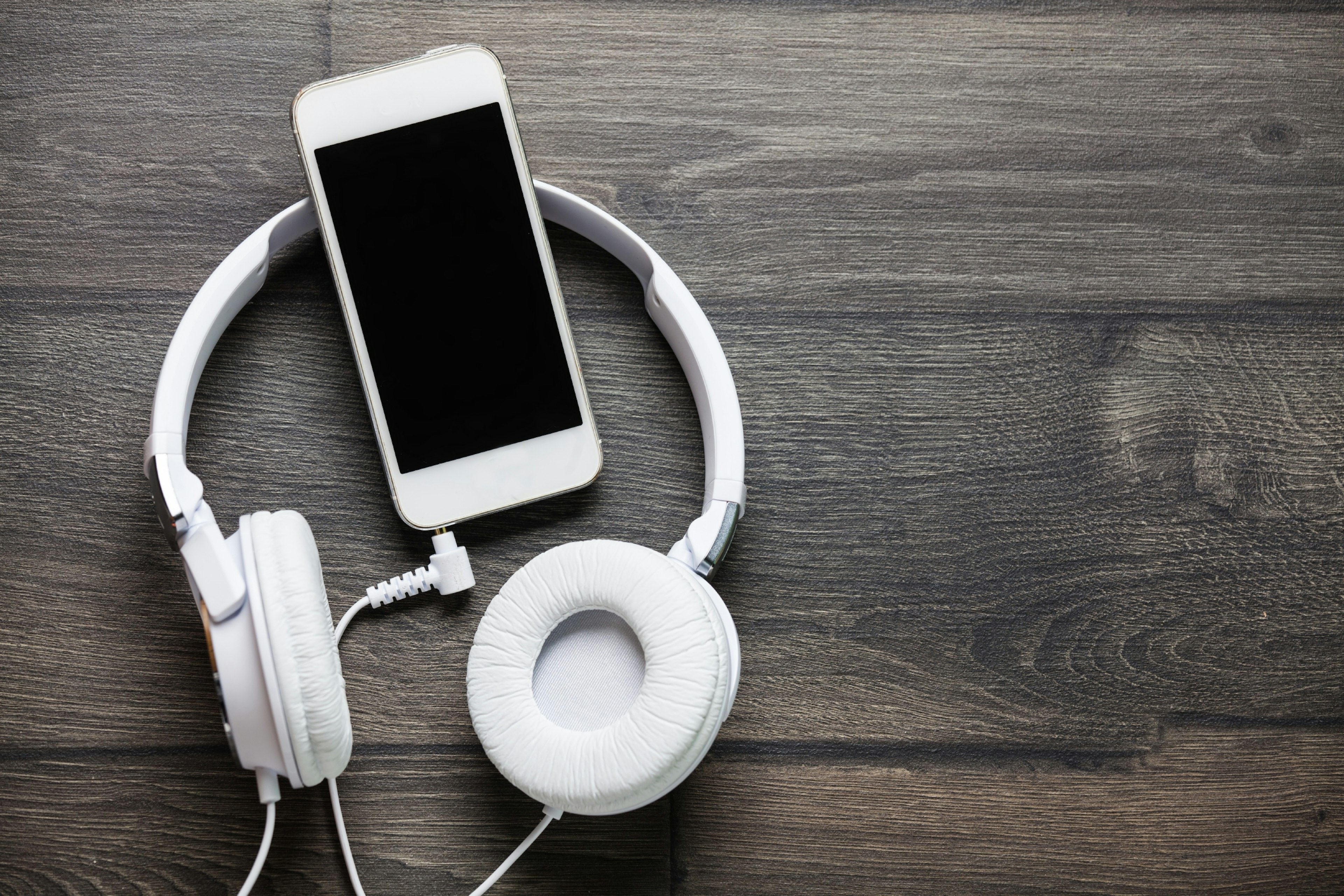 White headphones and phone on a wooden table.