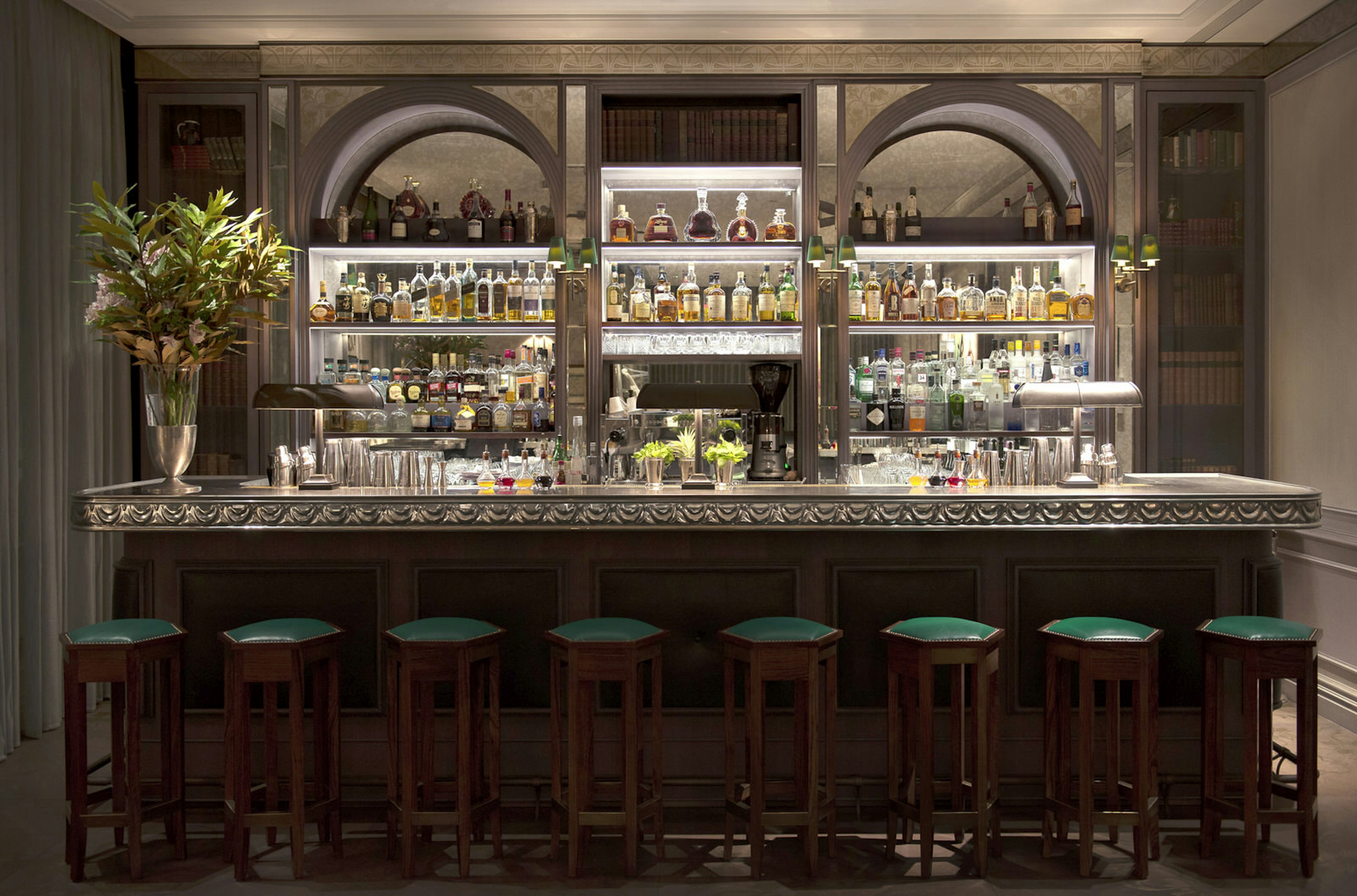 Wide shot of an ornate bar with wooden bar stools with green seats lined up beneath it © Library Bar