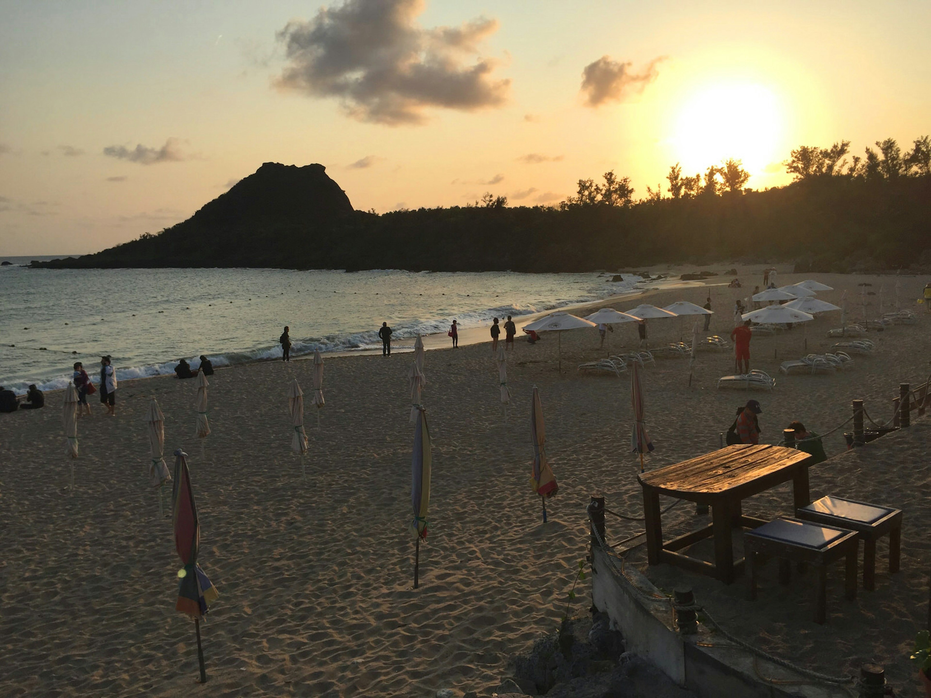 The sun sets over a small beach with a few people and some closed umbrellas. Superb swimming (and cocktails!), even in February, at Kenting's Little Bay Beach © Megan Eaves / ϰϲʿ¼