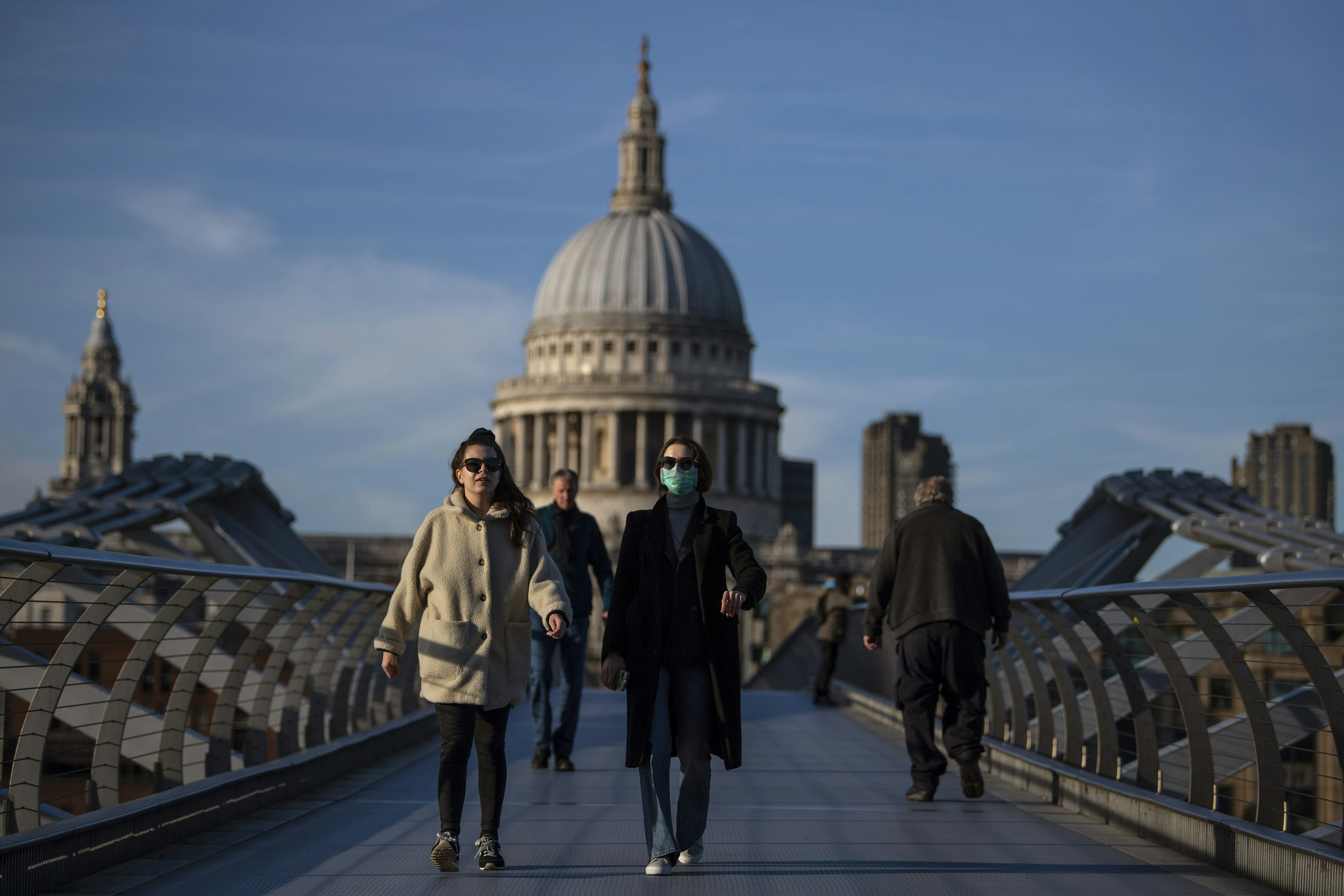 A woman crosses the Millennium Bridge in front of St Paul's Cathedral wearing a face mask during the COVID-19 pandemic in London.