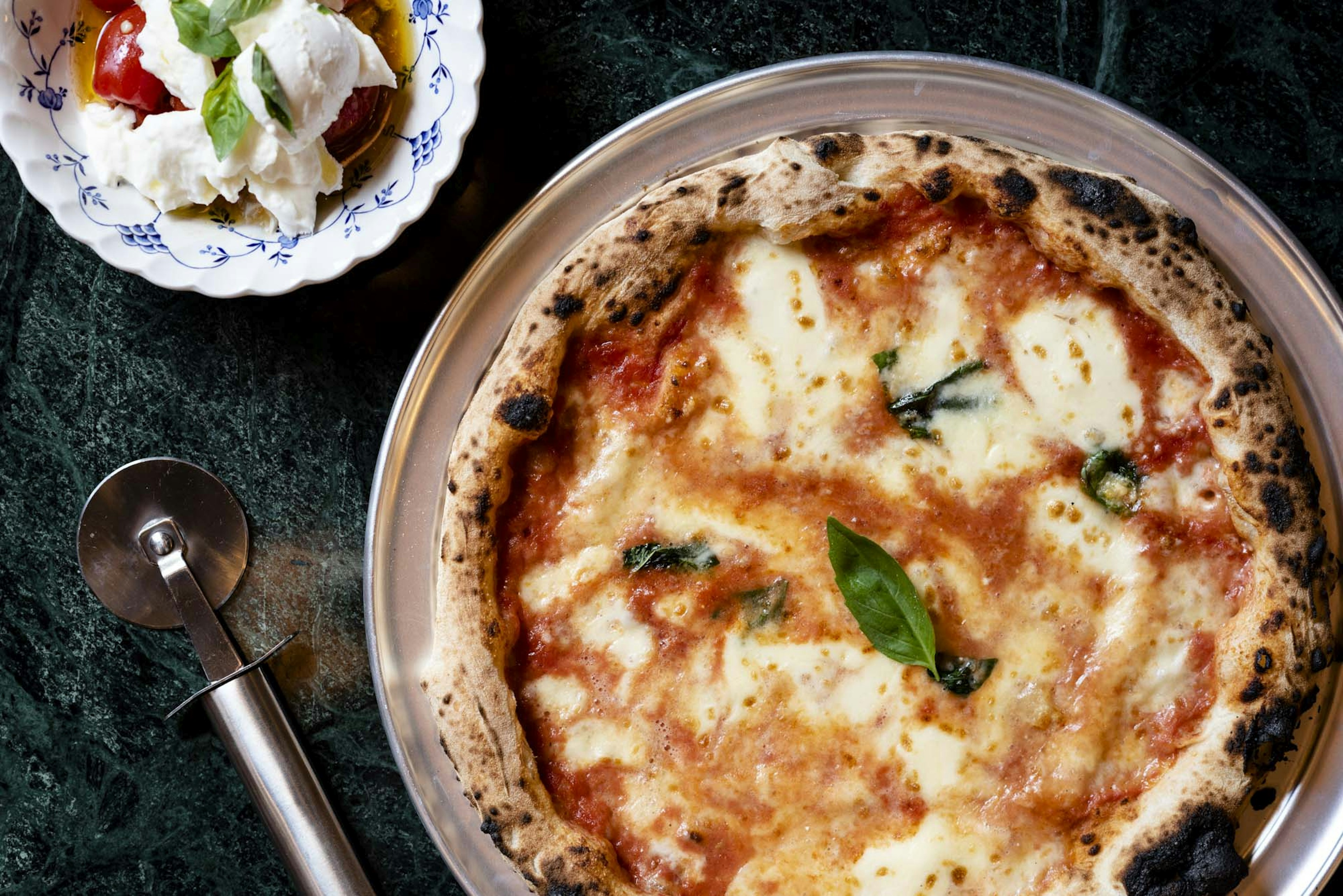 A picture of a classic Margherita ready to be cut into slices with a pizza roller