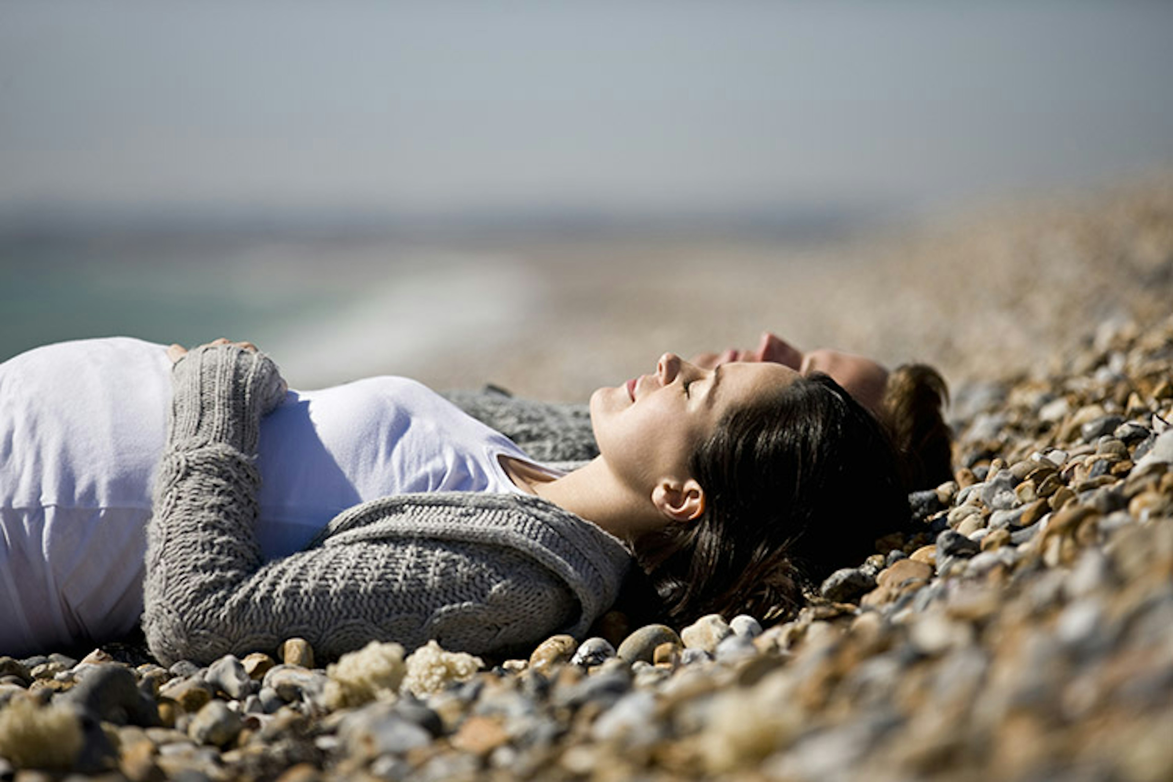 A couple lie back together on a pebbly beach enjoying their time