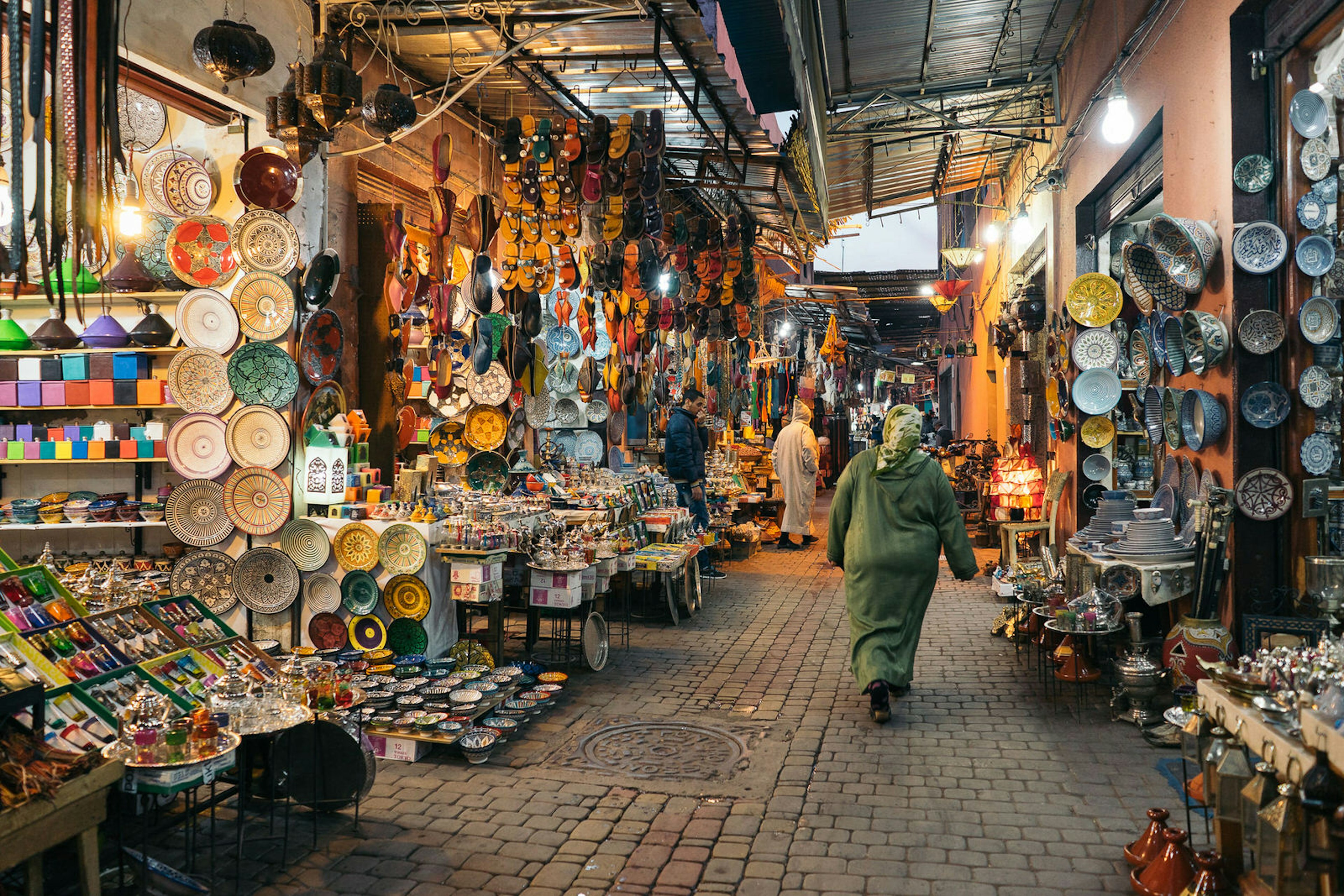 Moroccan woman walks through the medina of Marrakesh with stalls lining both sides of the walkway