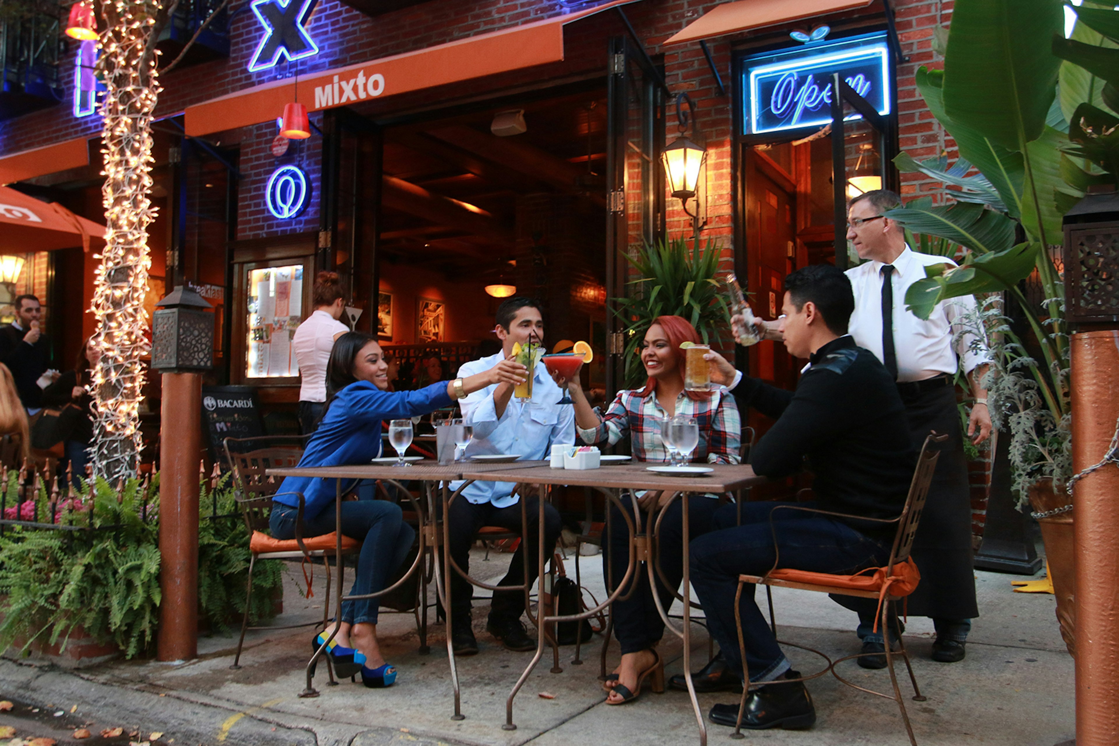 four twenty-somethings lift their glasses in a toast on the outdoor patio of Mixto in Philadelphia