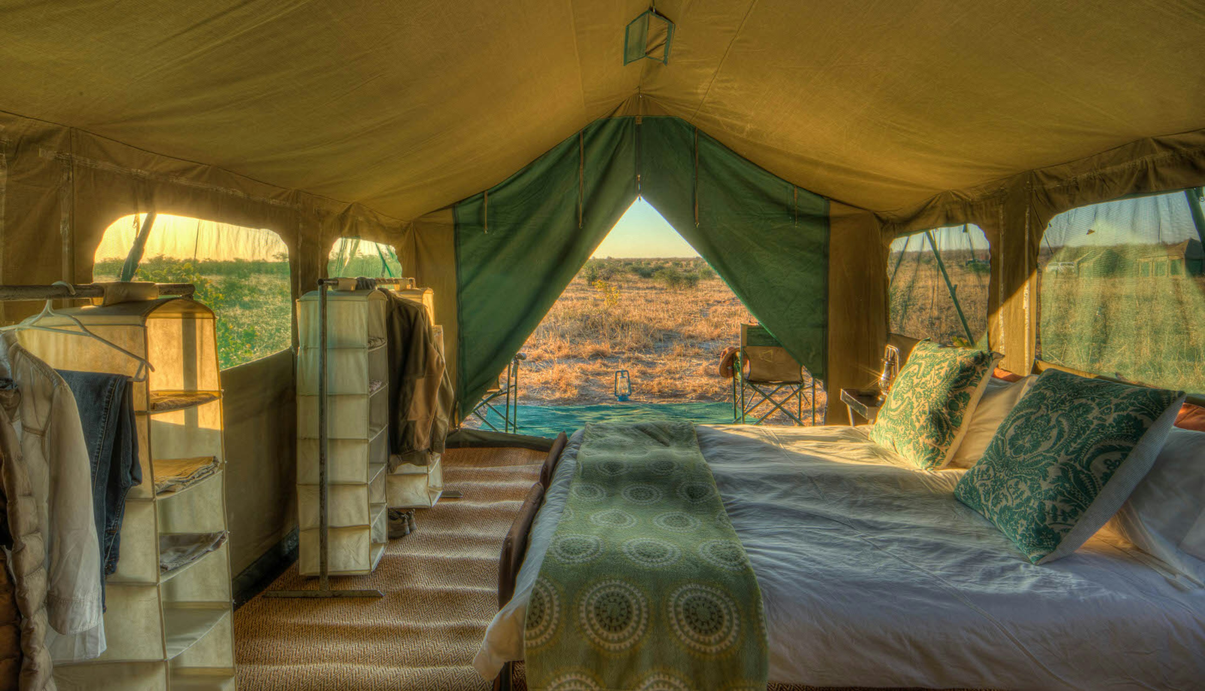 A large canvas tent in a mobile safari camp, with its zipper door open to let the early light in