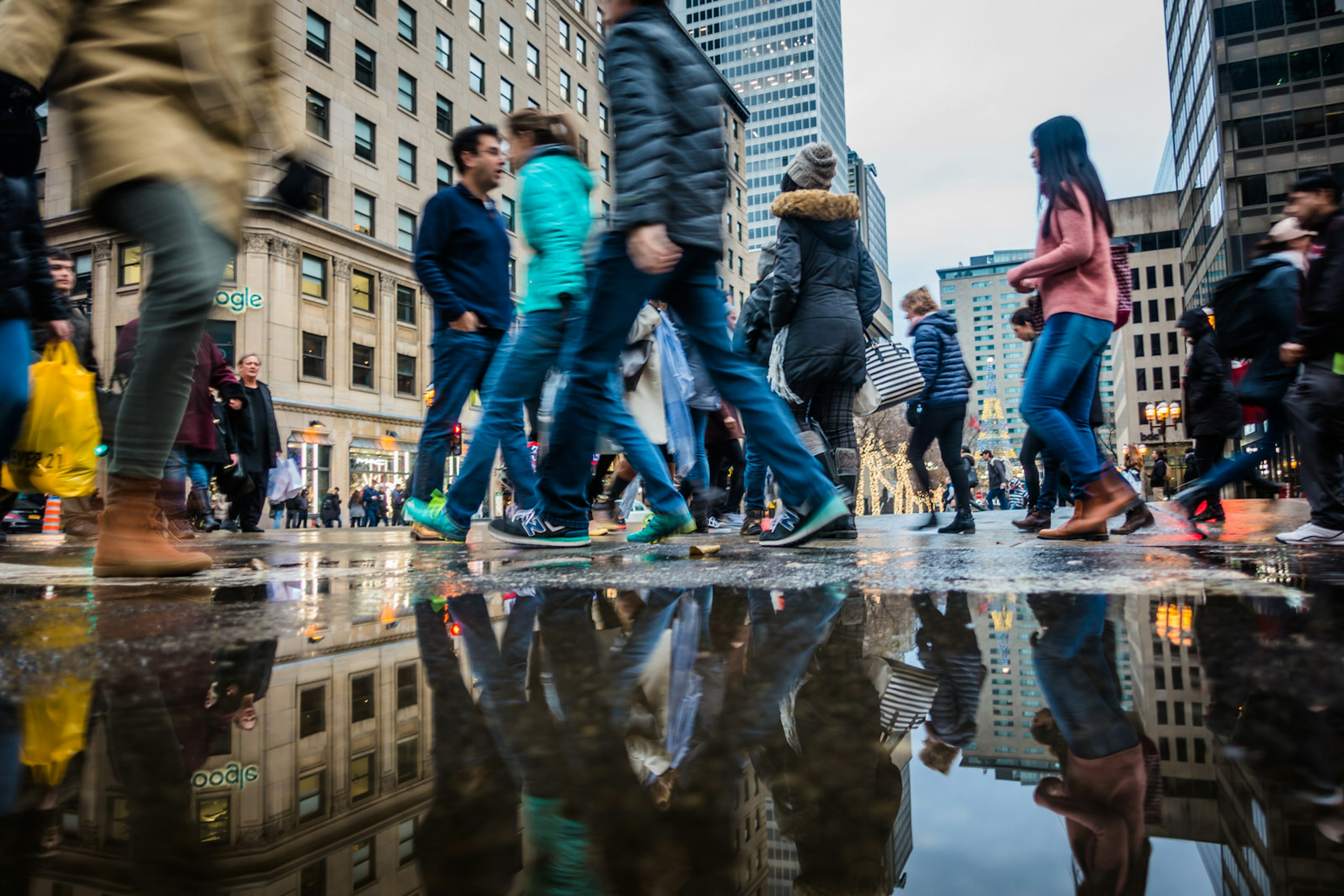 Walkers' legs reflected in a puddle in Montréal