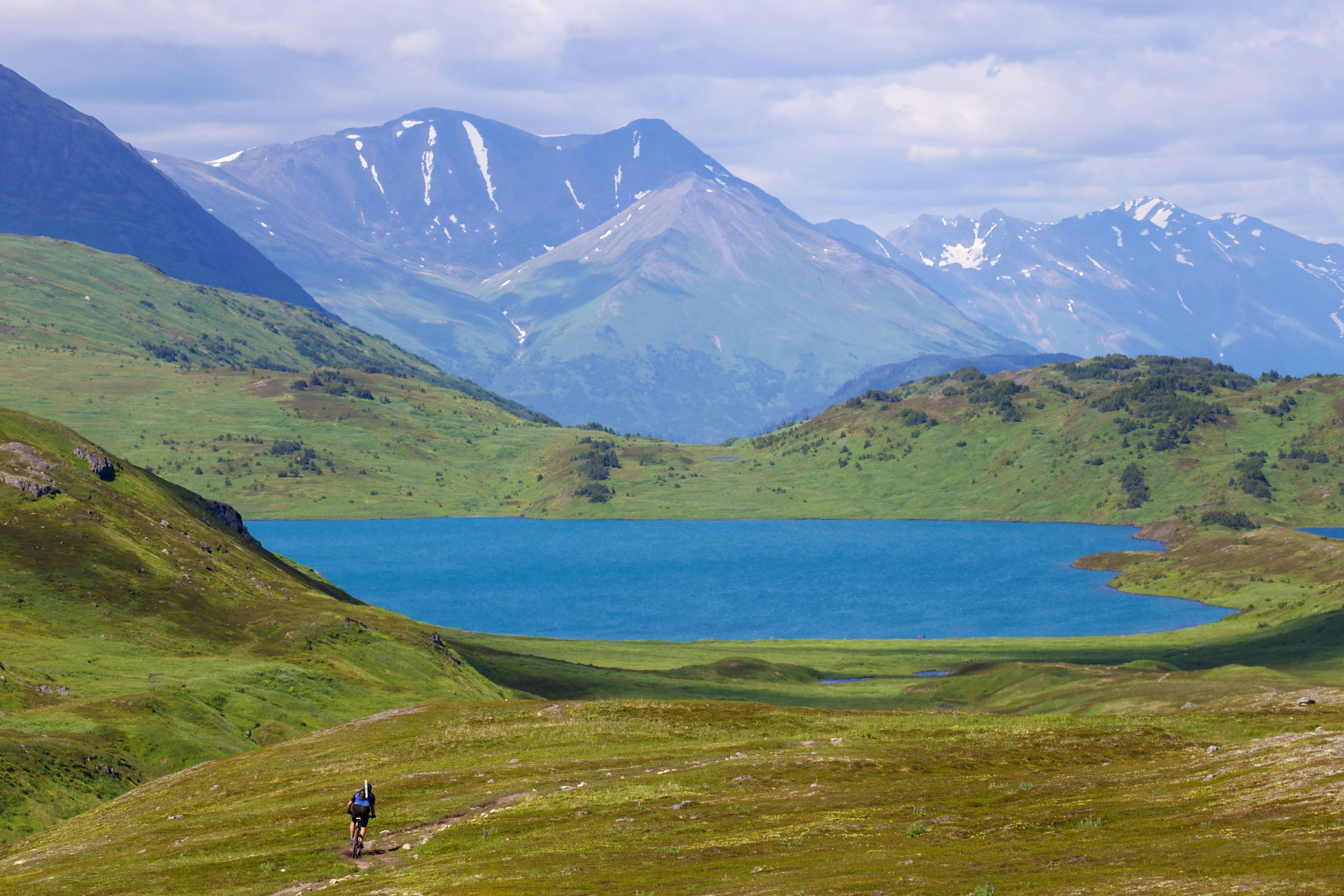 A mountain biker travels toward a lake surrounded by mountains