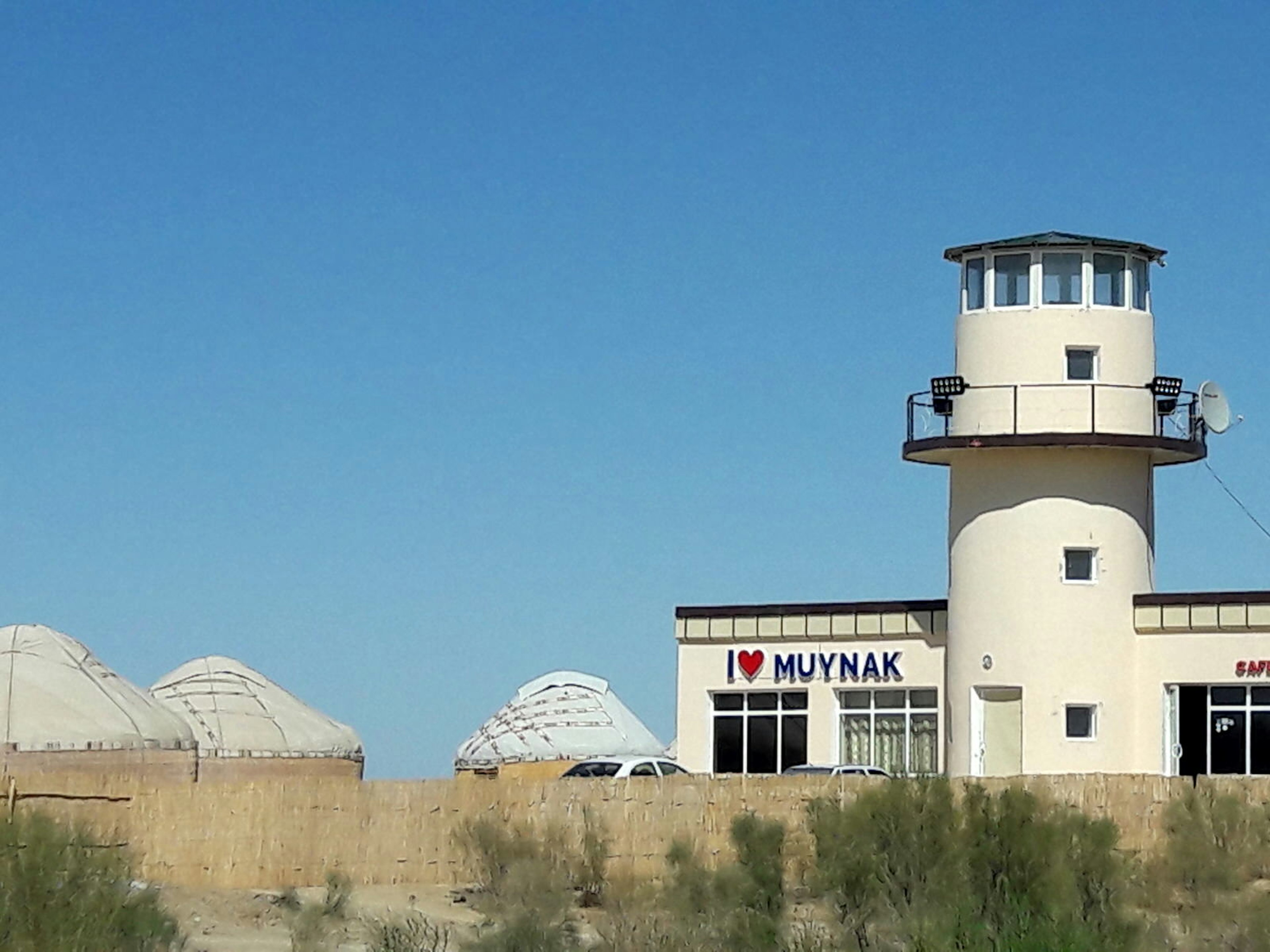 A white, round lighthouse stands next to a small building and several round yurt tents.