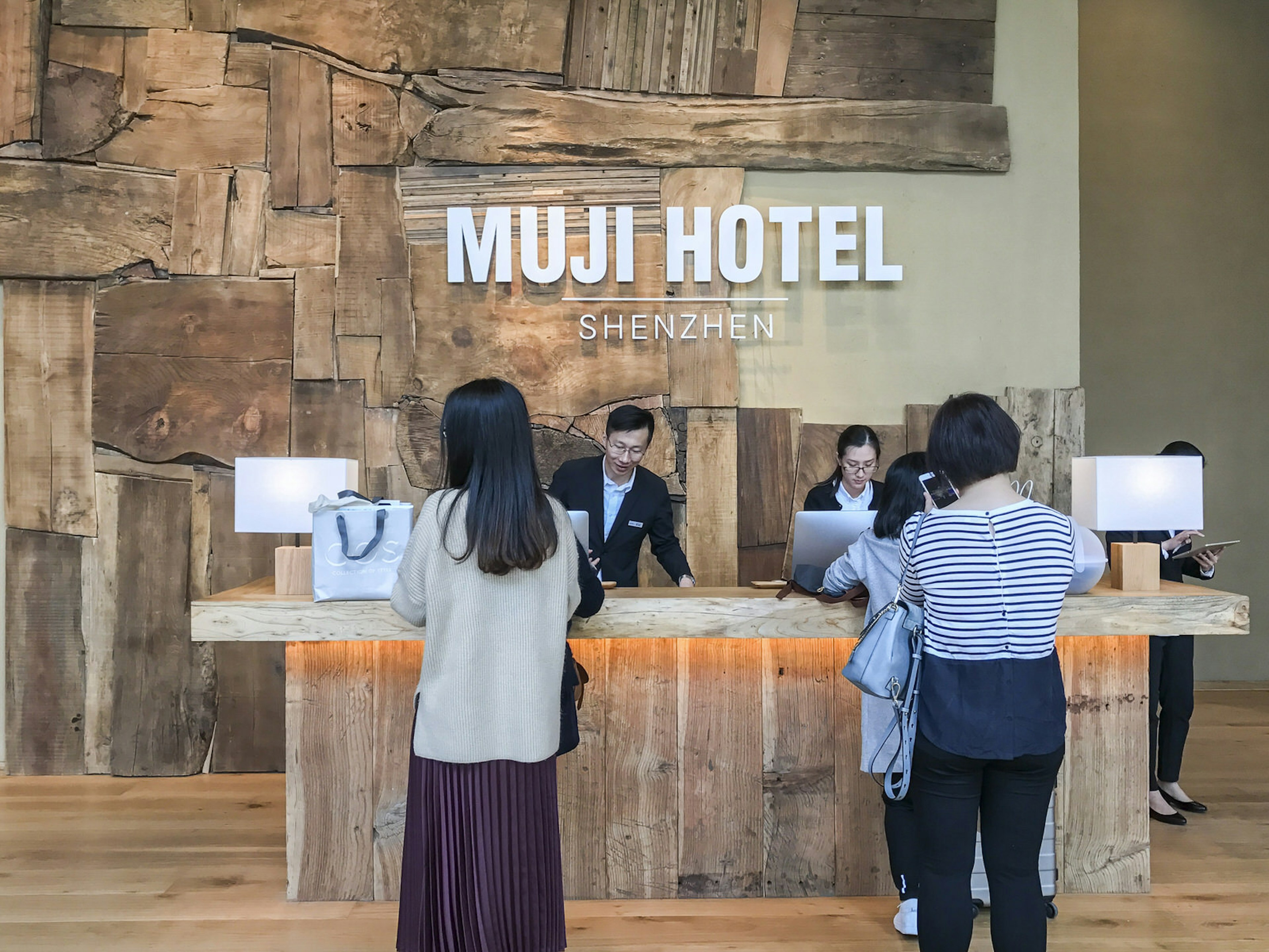 Guests stand in line to check in at a wooden desk with the Muji Hotel sign in big letters behind. Sleek Japanese design in Shenzhen: the Muji Hotel also houses a Muji store and diner © Cathy Adams / ϰϲʿ¼