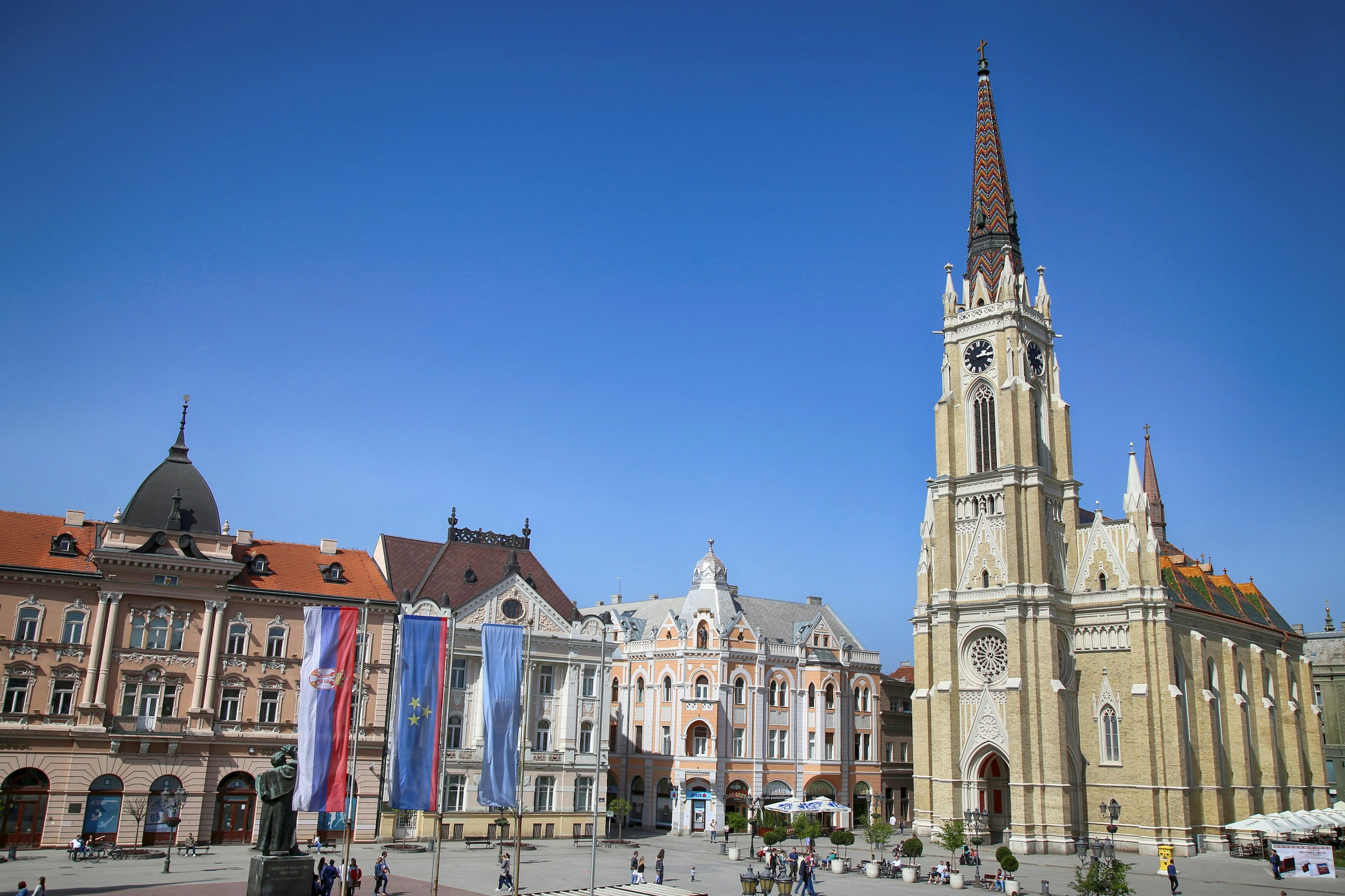 A church dominates once side of a square. It has a tall spire with detailed colourful tilework on it