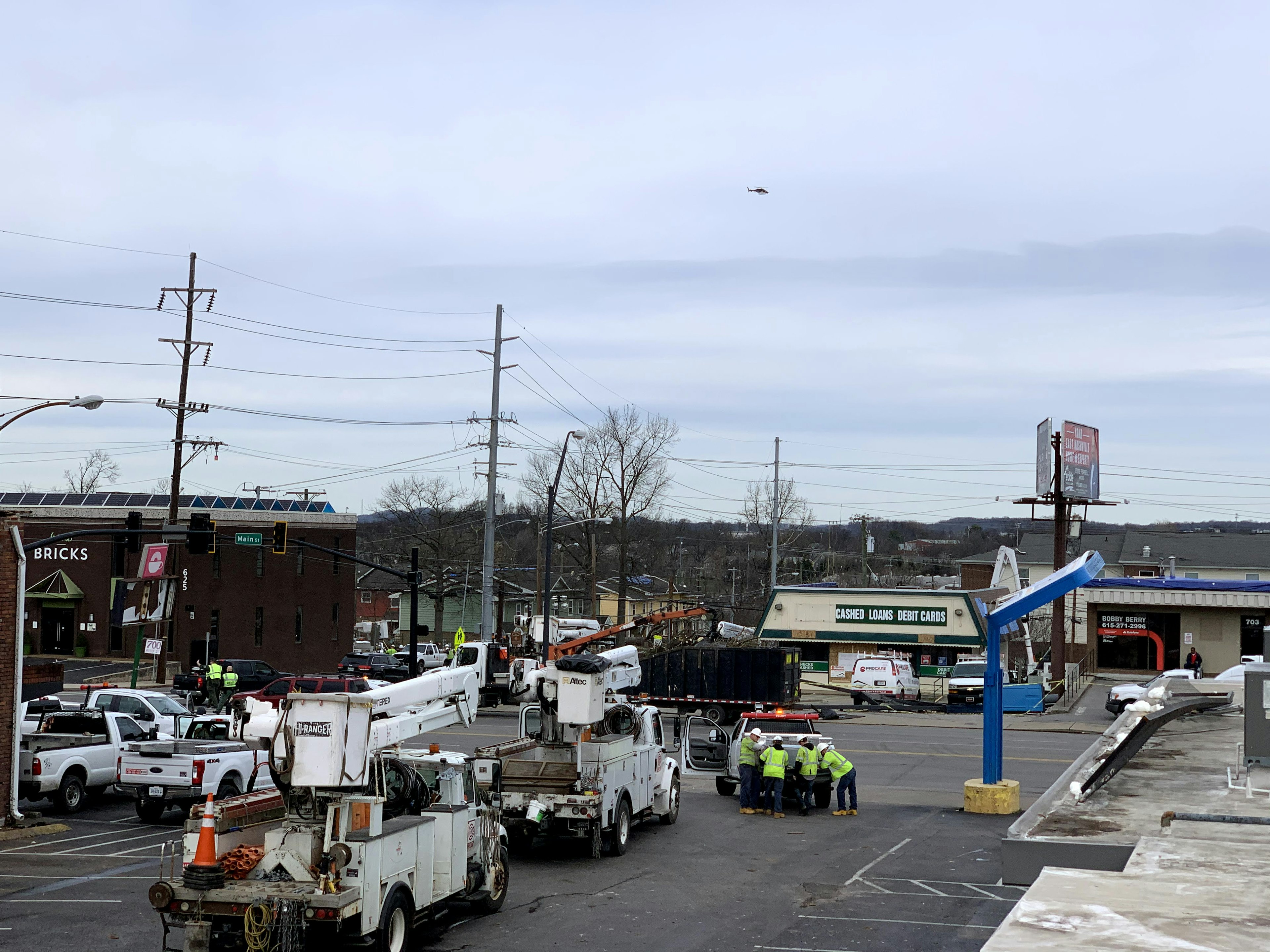 Two utility trucks line up behind a pickup with crew in yellow safety vests in the East Nashville neighborhood near Main Street after a tornado blew through the Five Points business district