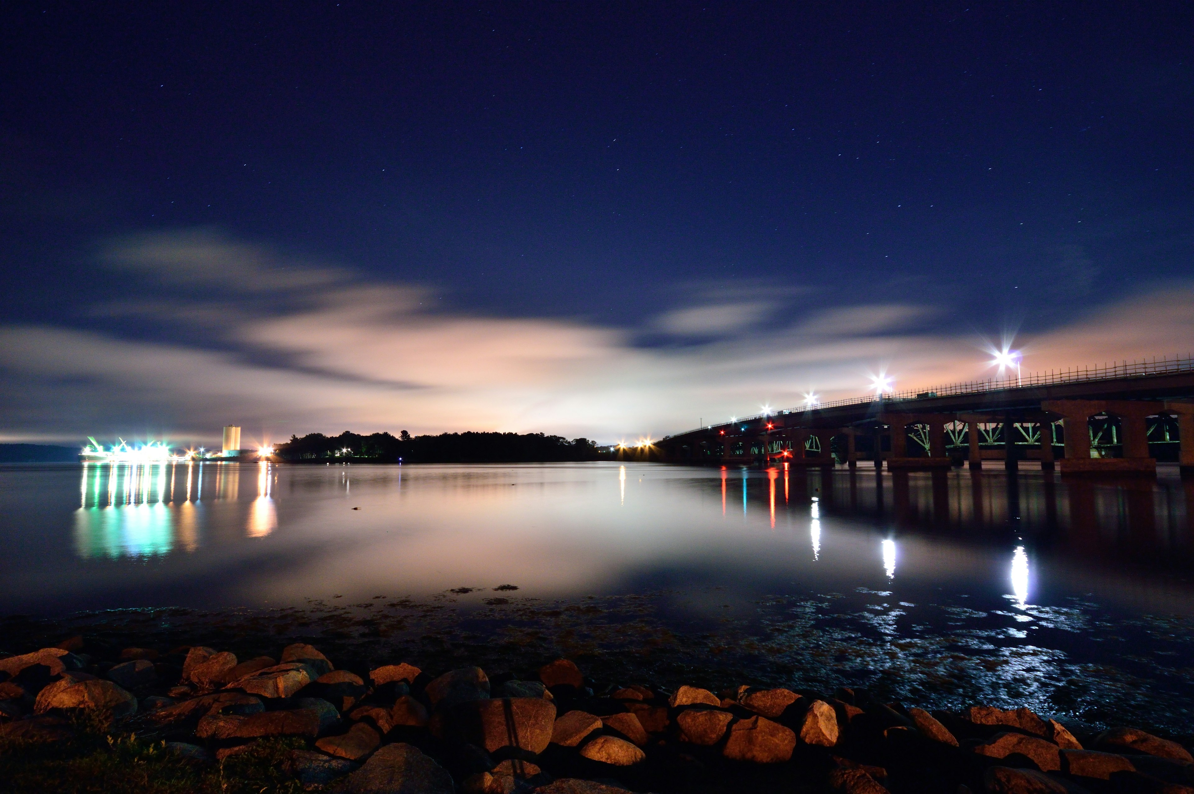 The general sullivan bridge connects the two landmasses of Portsmouth and Dover. This normally high traffic waterway is relatively empty this evening as the bright lights of an unloading cargo ship reflect off the calm waters of the piscataqua river.