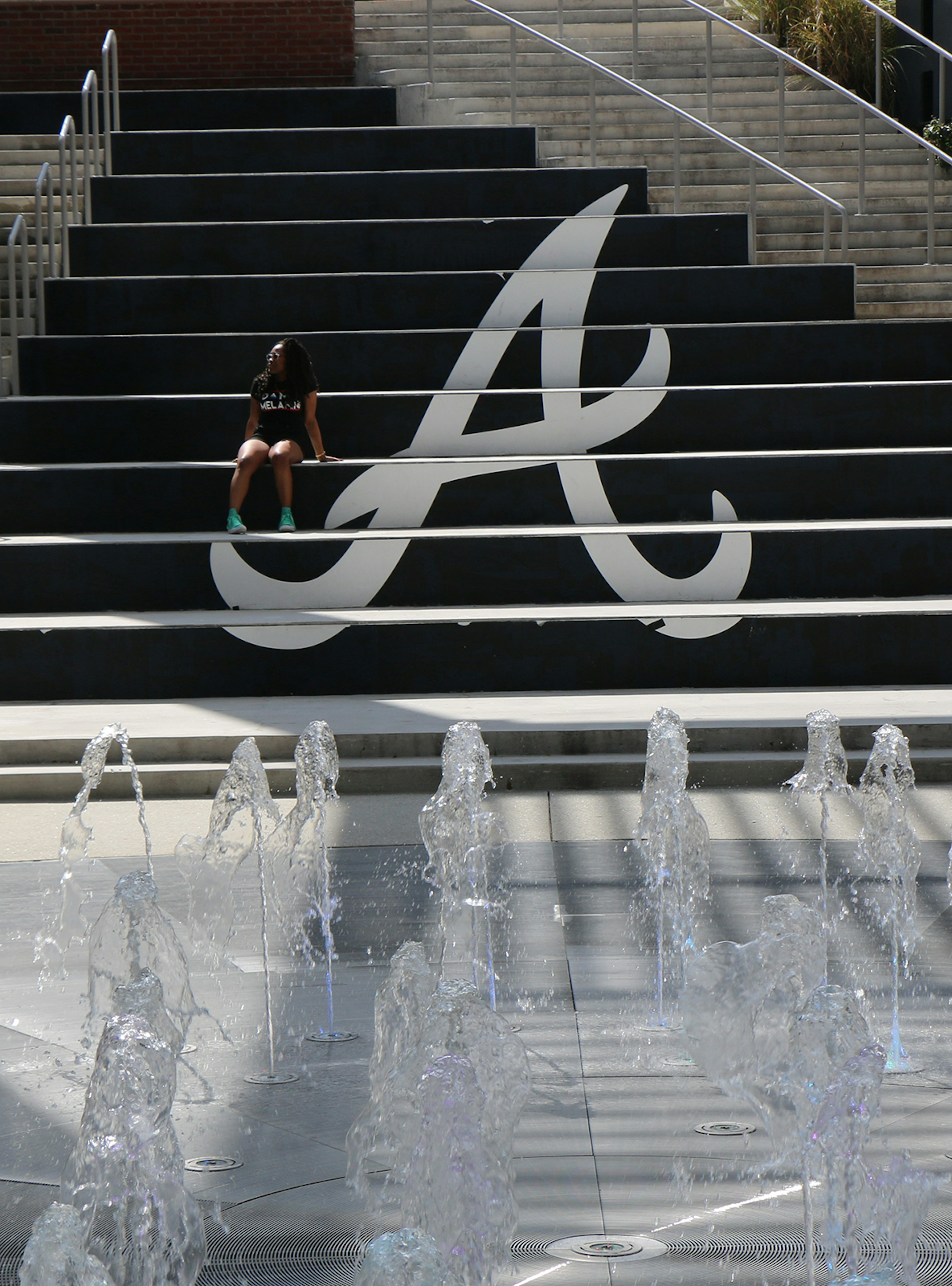 Long shot of woman sitting on staircase painted with the letter 'A' for the Atlanta Braves, with fountains in the foreground