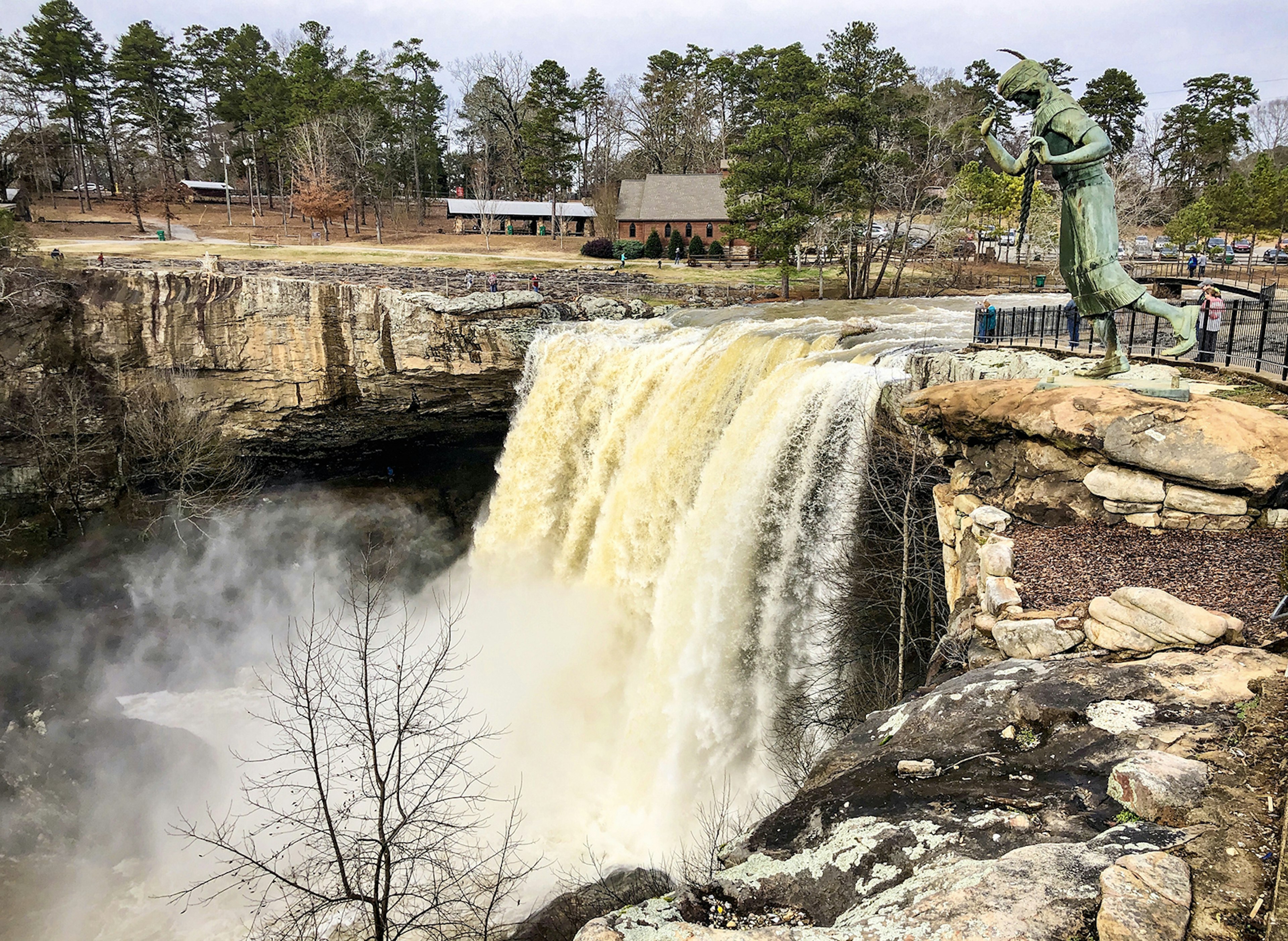 A waterfall pours down into a limestone gulley in North Alabama. The statue of a Native American woman is just to the side.