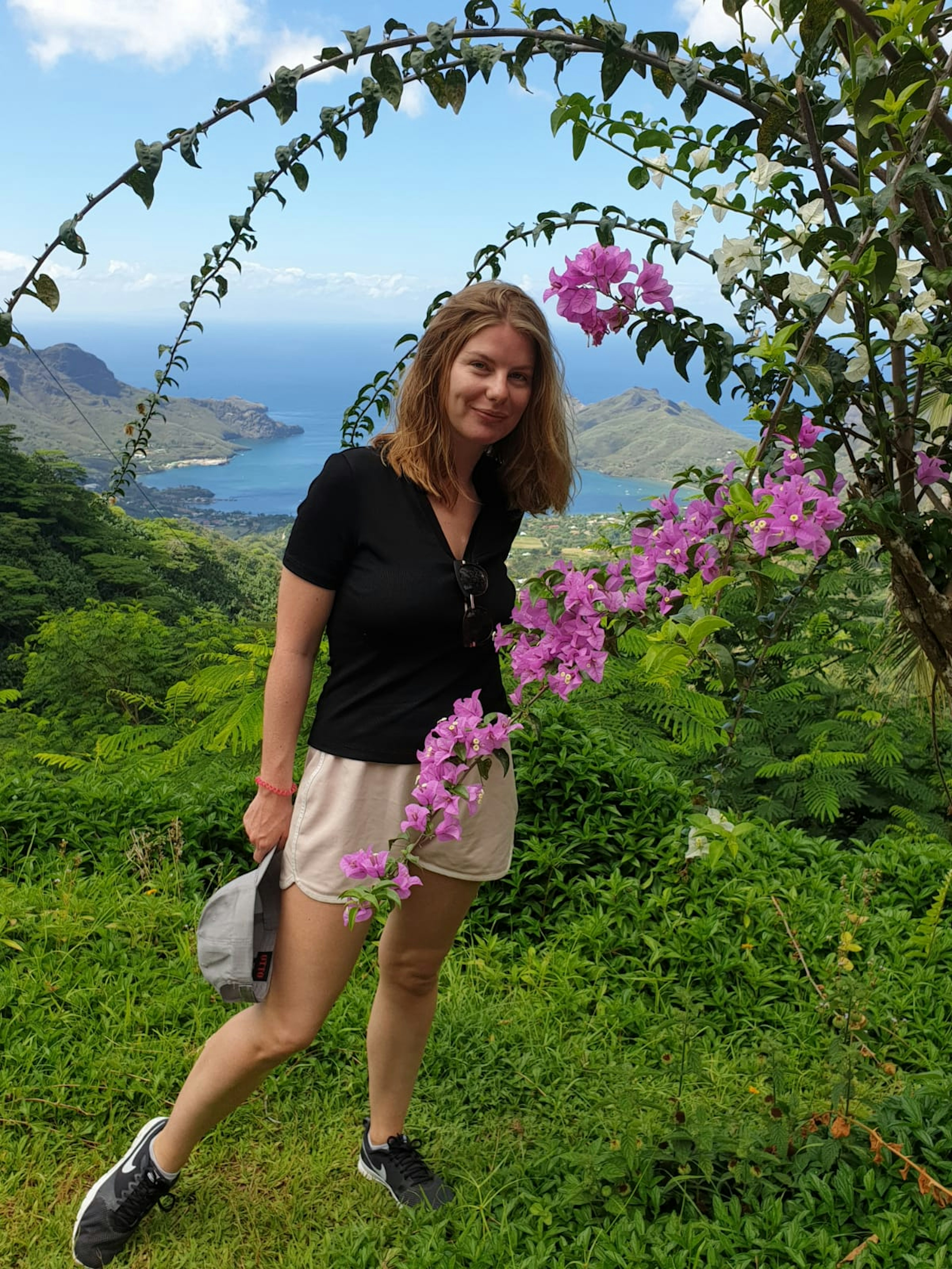 Caroline stands on a hilltop in Nuku Hiva with the sea visible behind her