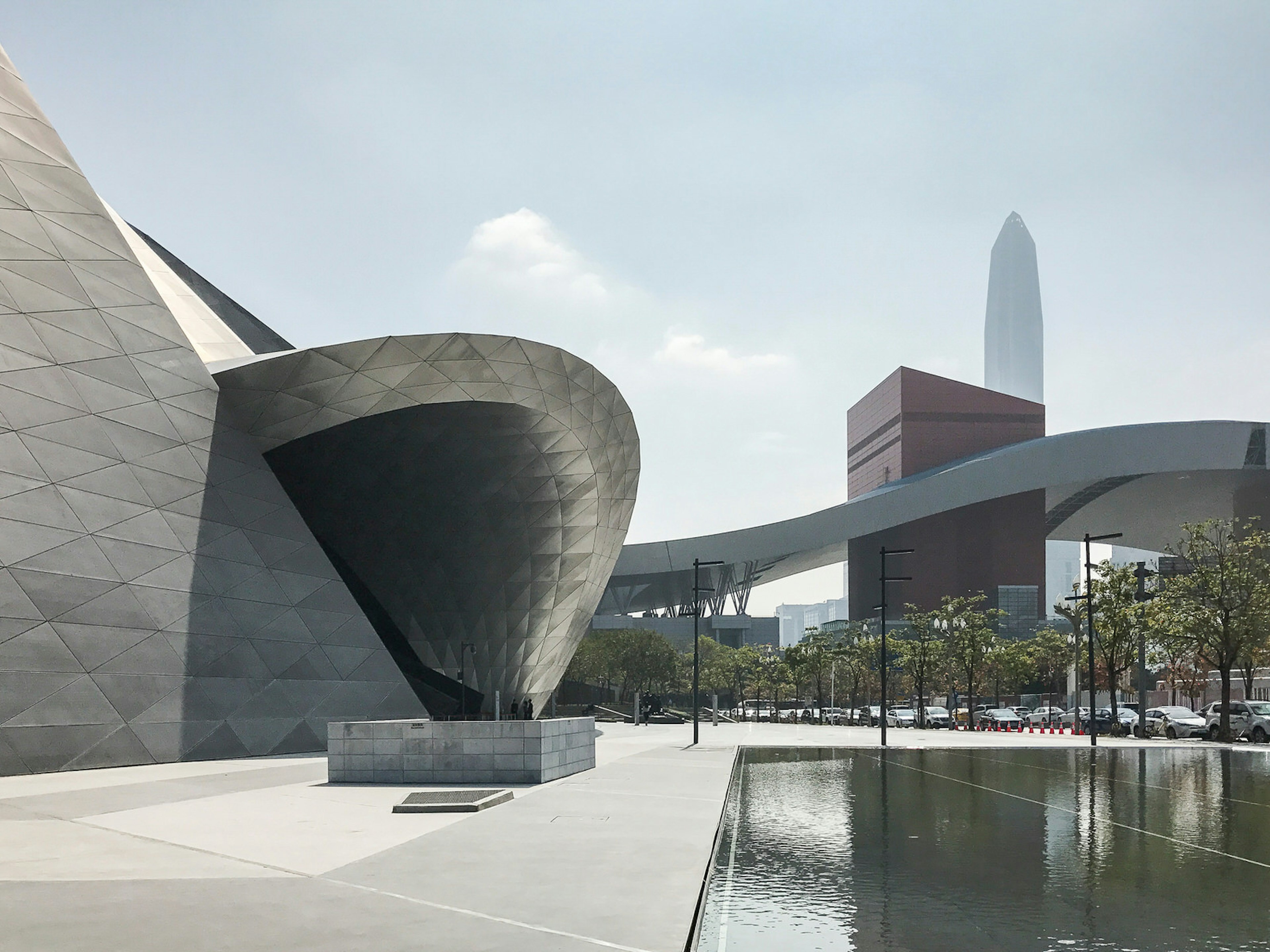 A sleek, metal rounded building next to a concrete-basin pond with a skyscraper in the distance; The spaceship-like Museum of Urban Art and Contemporary Planning © Cathy Adams / iBestTravel