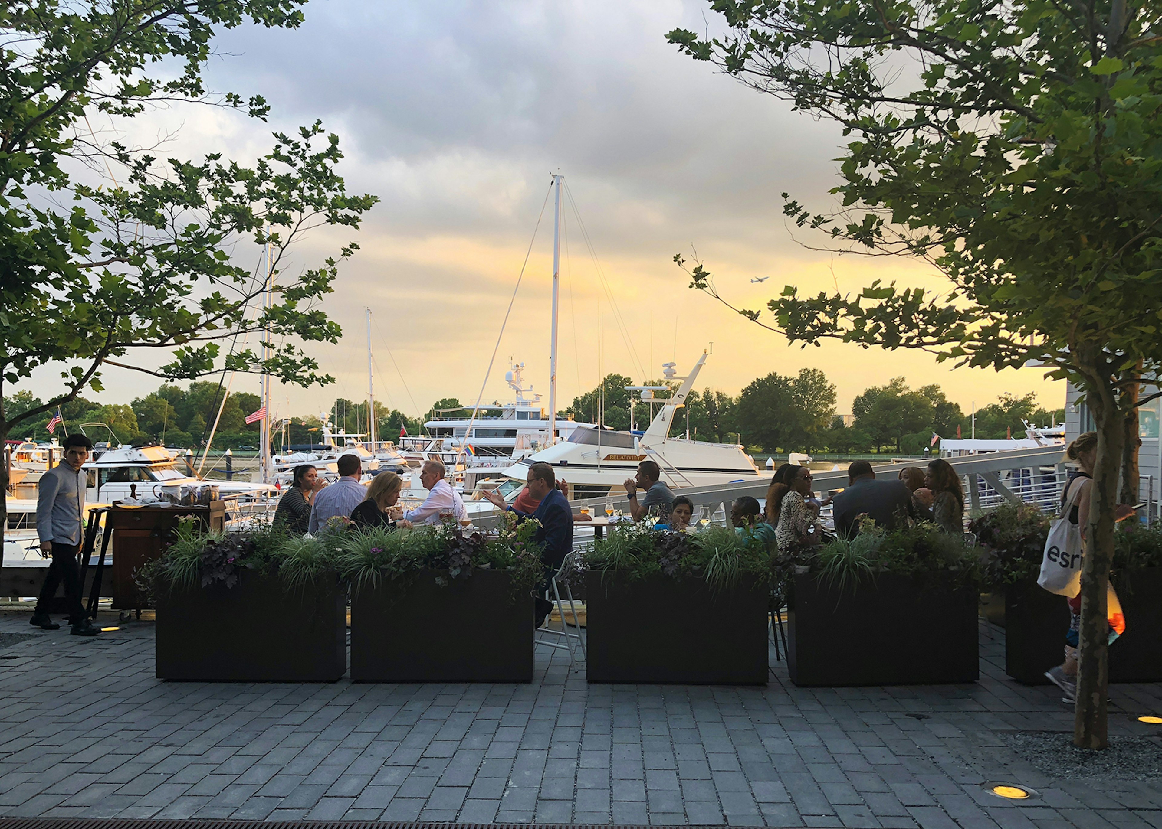 People dine at outdoor tables as the sun sets, with boats parked in the marina behind them © Trisha Ping / Lonely Planet