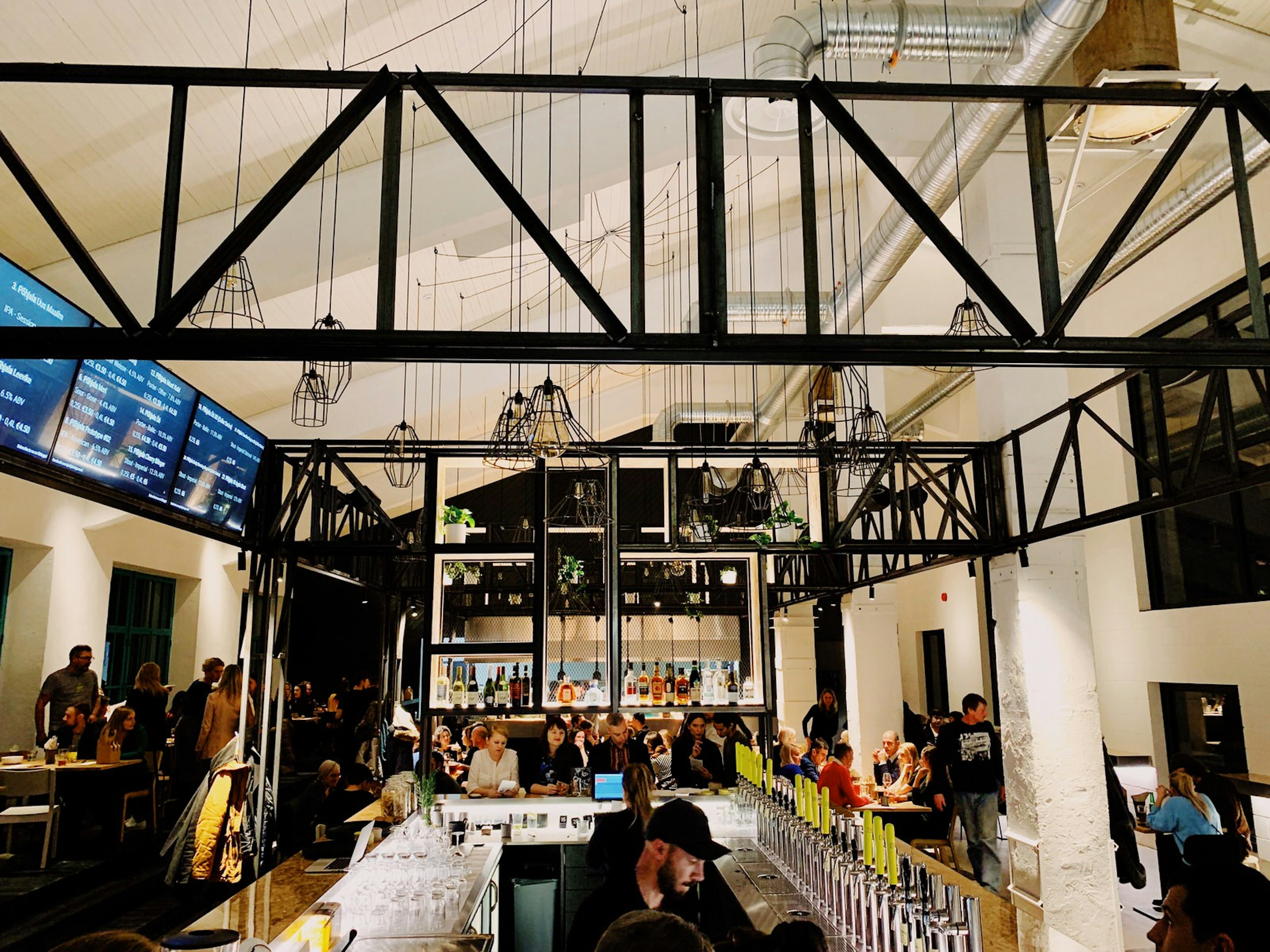 A long bar with beer taps in a room with vaulted ceilings and digital menus above the bar