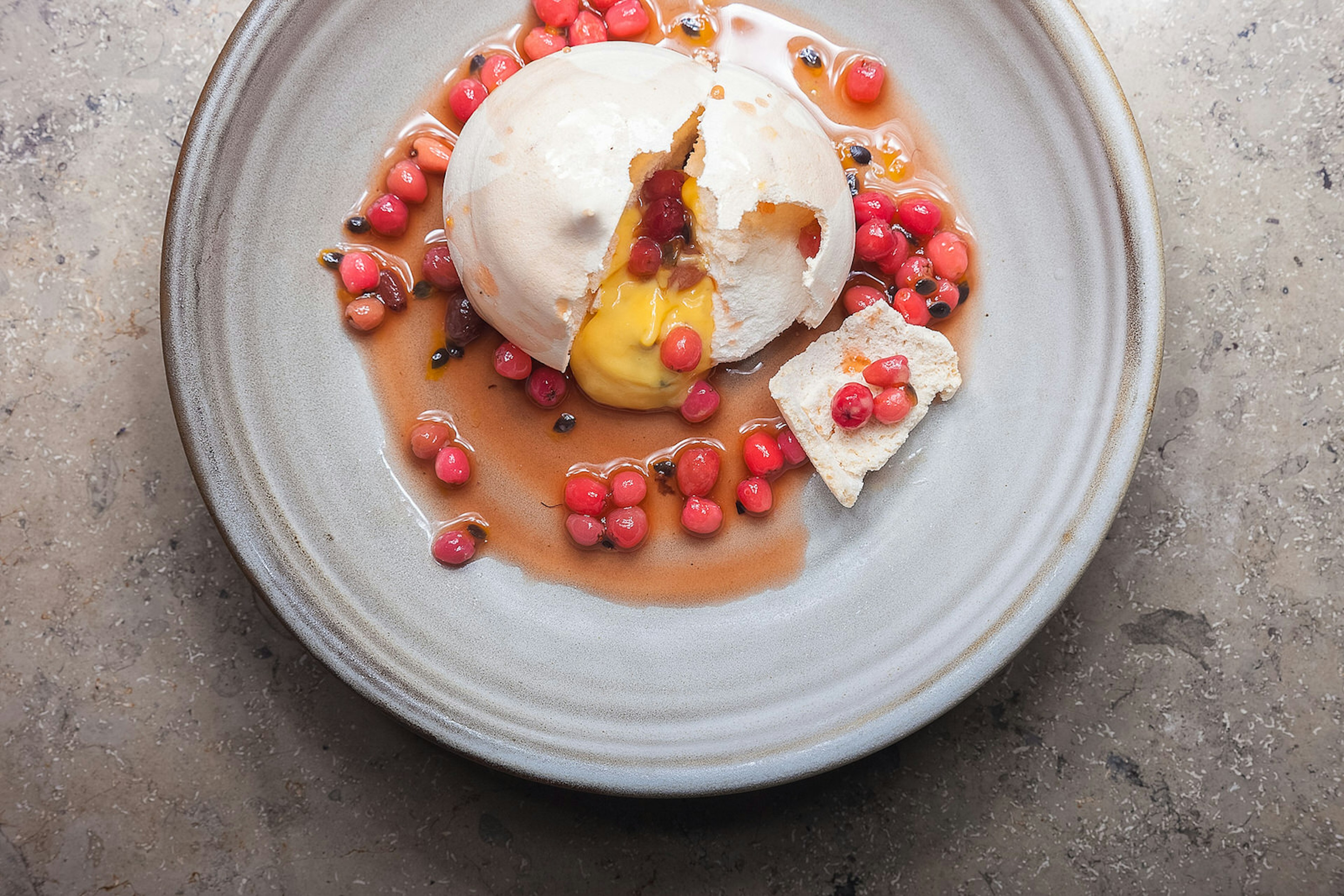 A saucy looking riberry and passion fruit pavlova from Harvest Newrybar with a passion fruit curd on an earthware plate