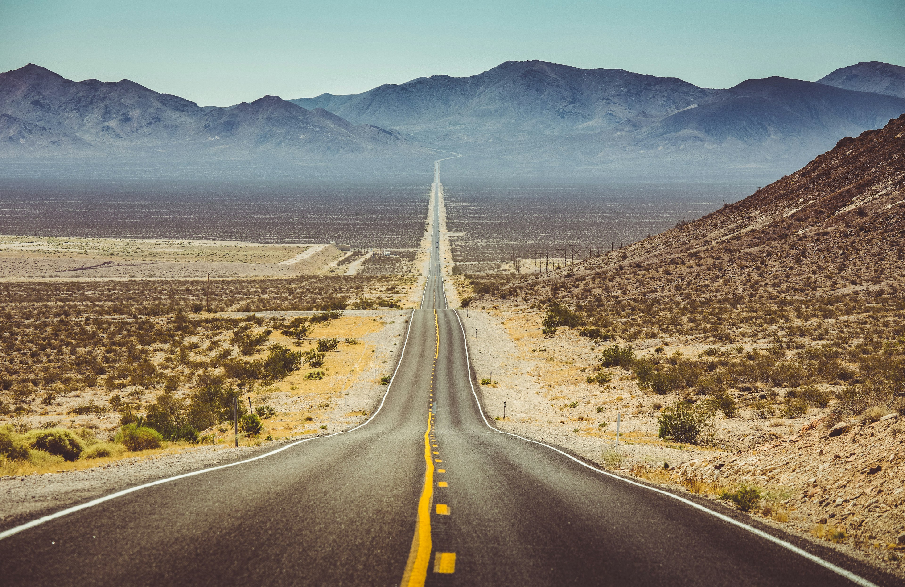 A long and straight road goes through a dry landscape toward mountains