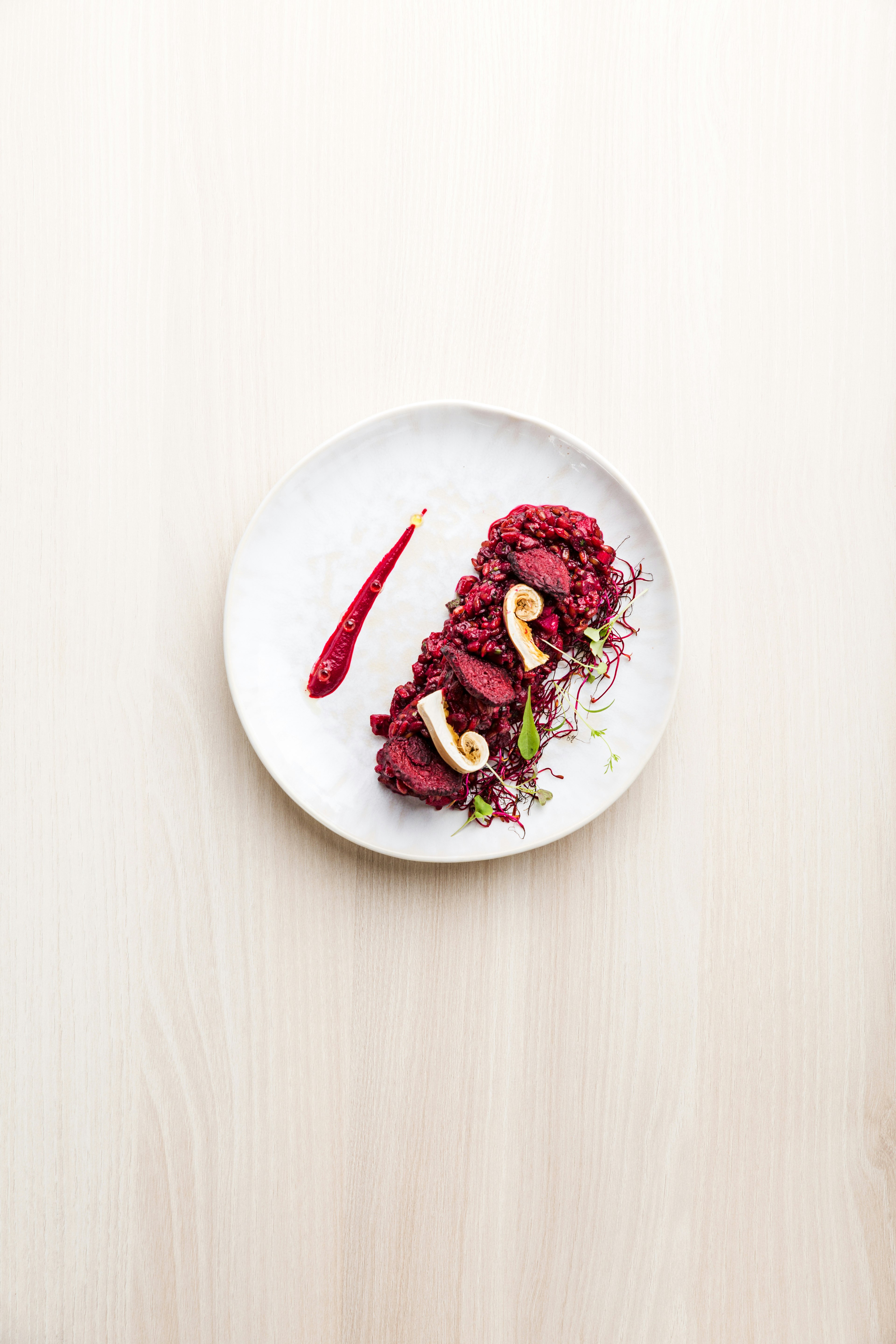 A gourmet meal is laid artistically on a white plate. The ingredients are predominantly crimson in colour, but there are some slices of mushroom and green leaves as a garnish.