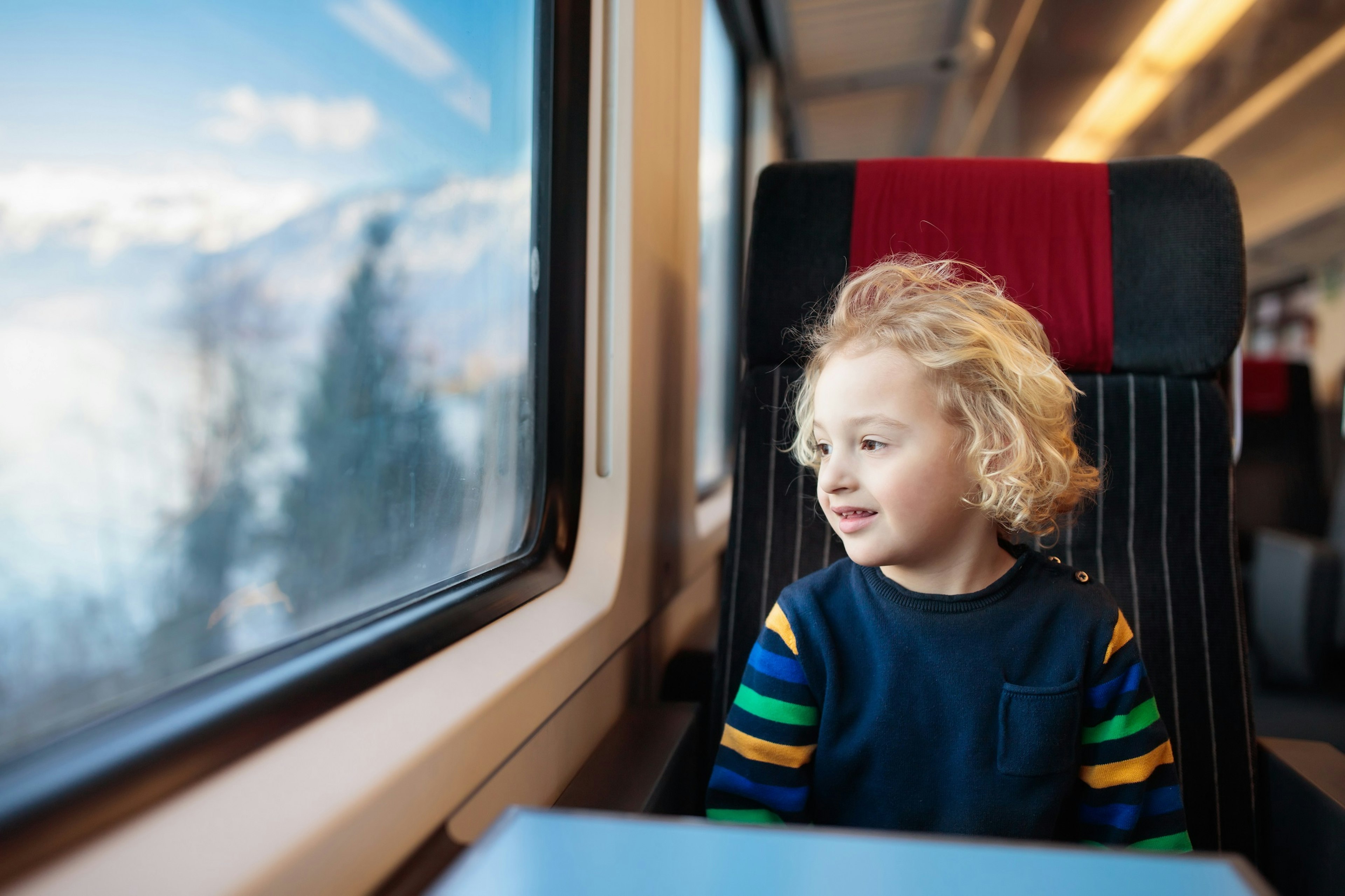 A young child sitting in a train seat looks out delightedly at a snowy landscape.