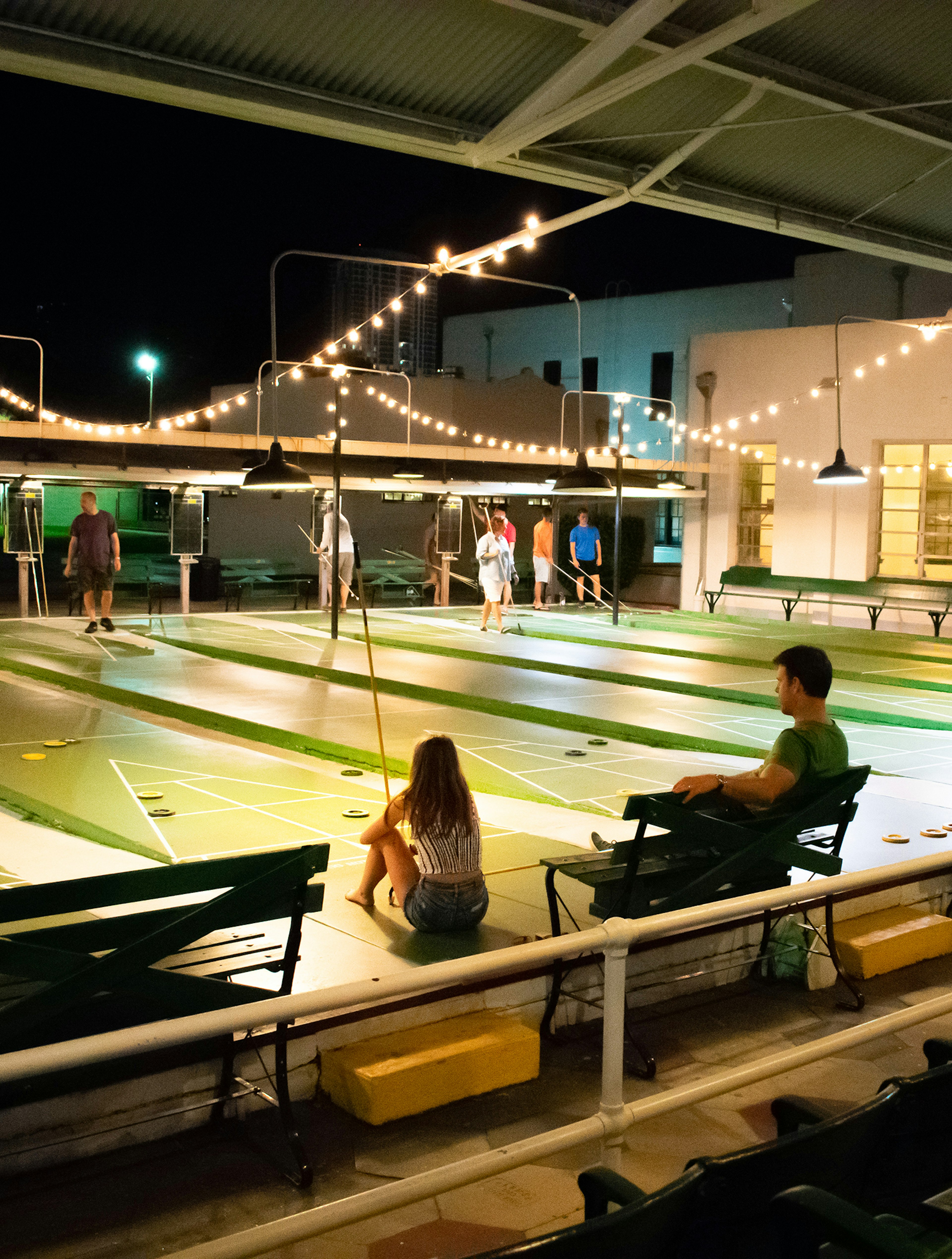 Group of people playing shuffleboard in St Petersburg. The club is open air and lit with string lights as it is night time © Abbey Cory / Lonely Planet