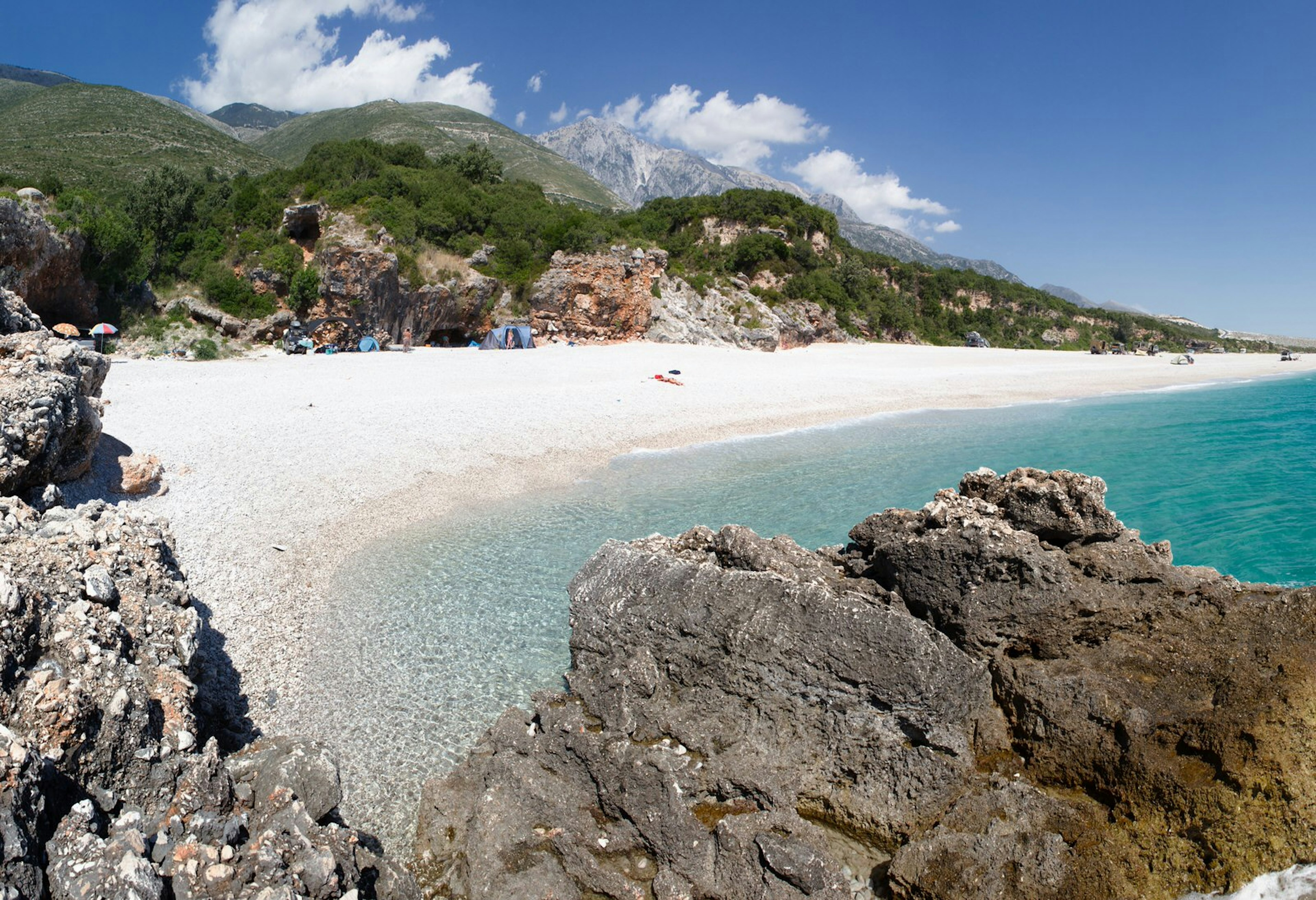 Pebbly Palasa beach with green hills behind it and mountains in the distance