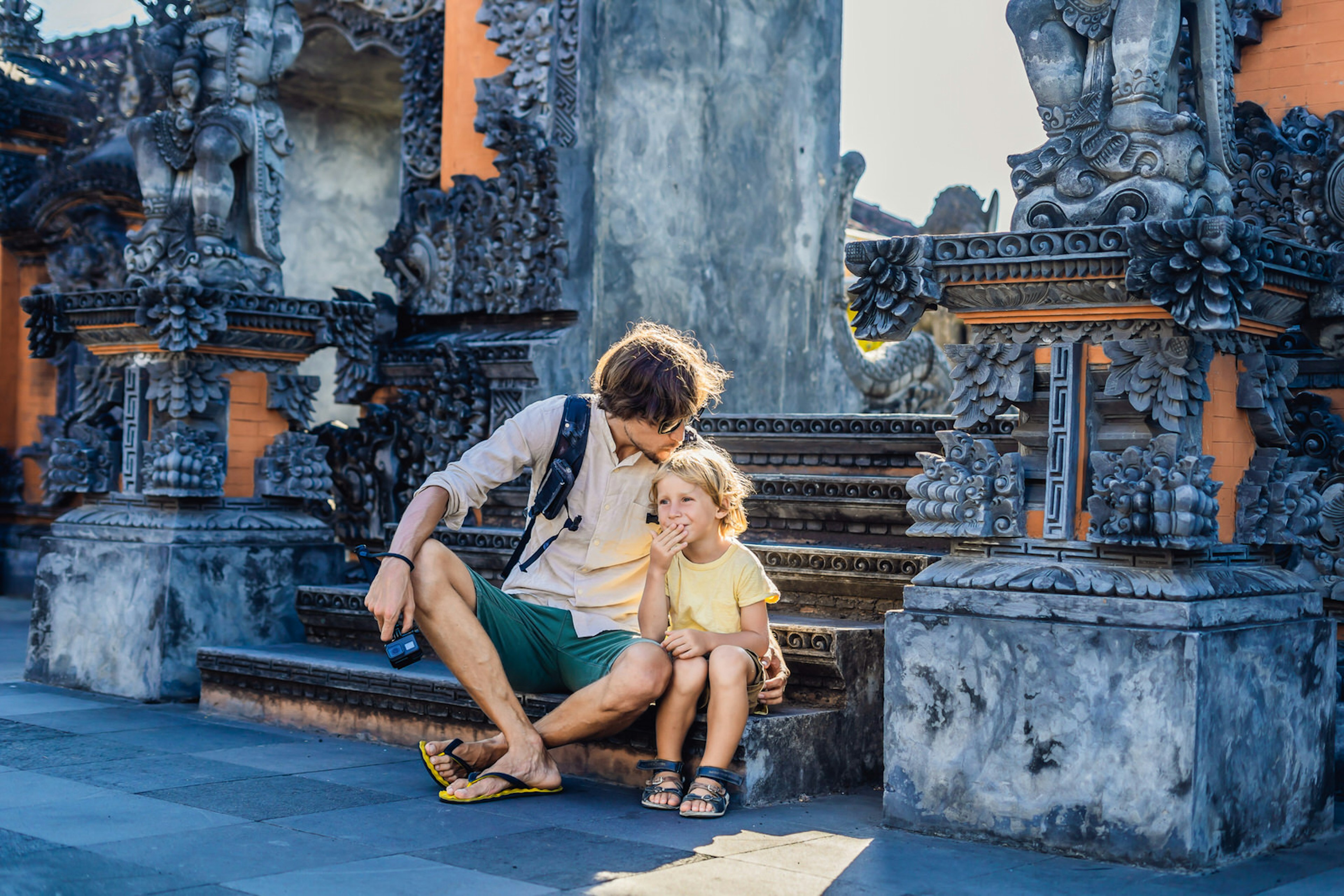 A father and son enjoy an affordable family vacation, on the steps of a temple in Bali