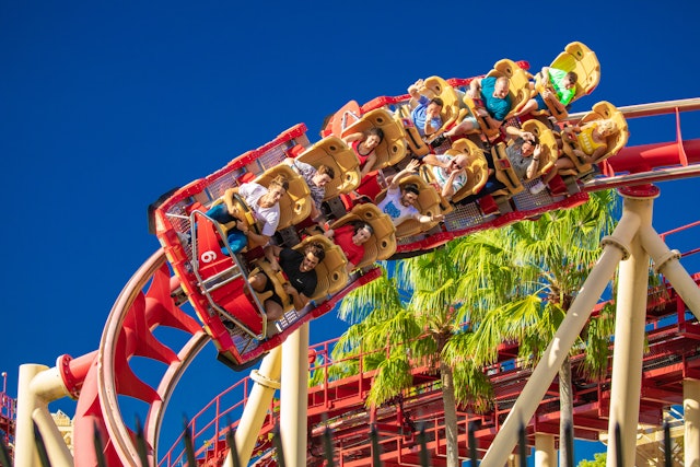 People riding a red roller coaster against a blue sky