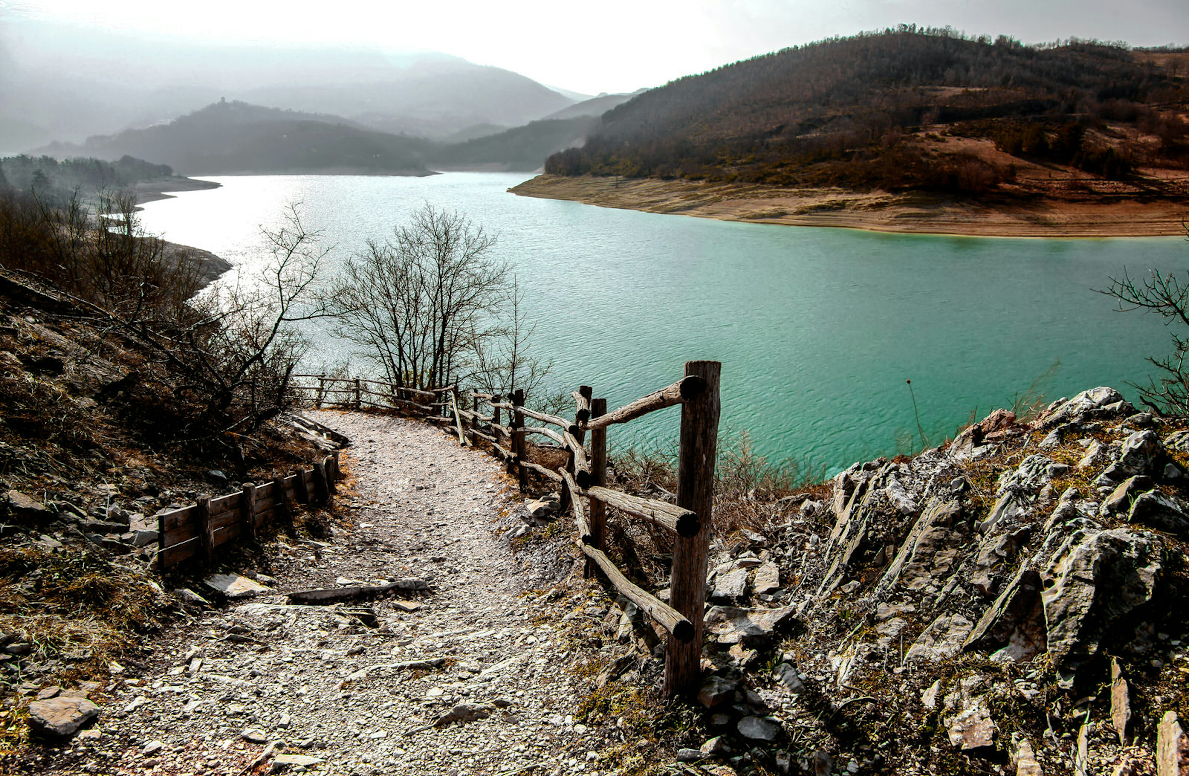 A view of a pathway leading down to the turquoise waters of Lago di Fiastra in Italy with green mountains in the background