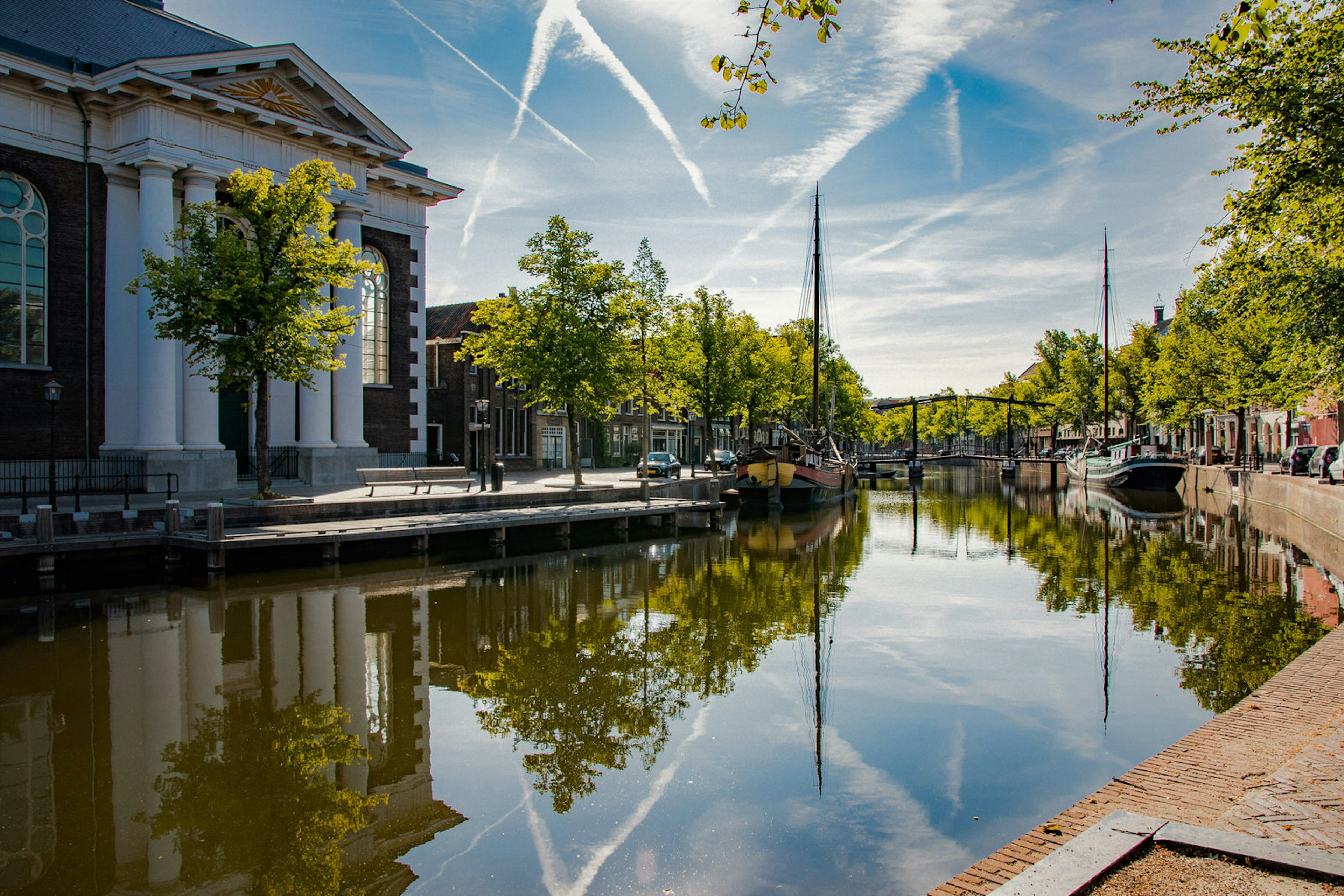 A canal in Schiedam with a bridge, trees and a white, grand-looking building visible