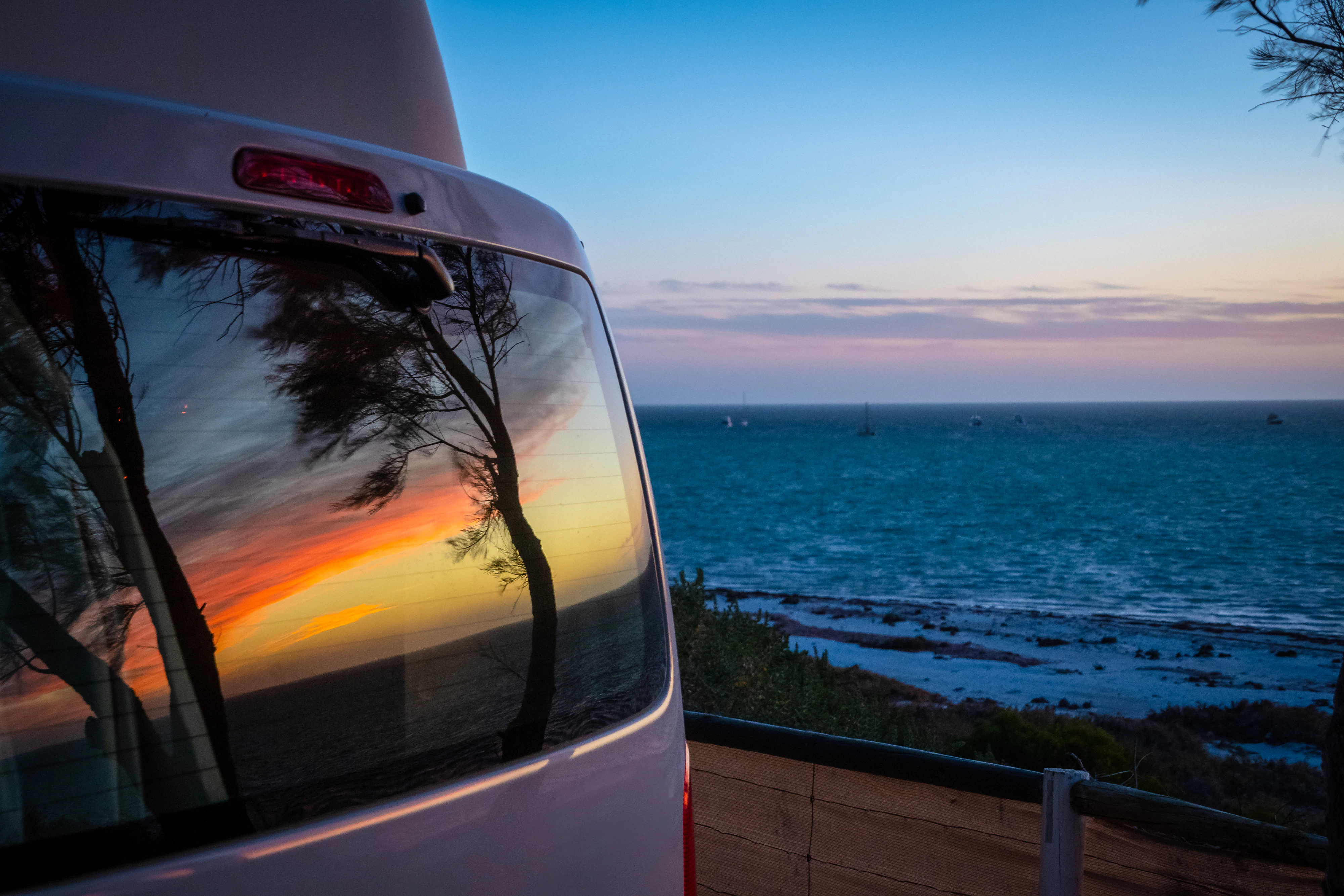Reflection of tree silhouettes on campervan window in front of Indian Ocean in Australia