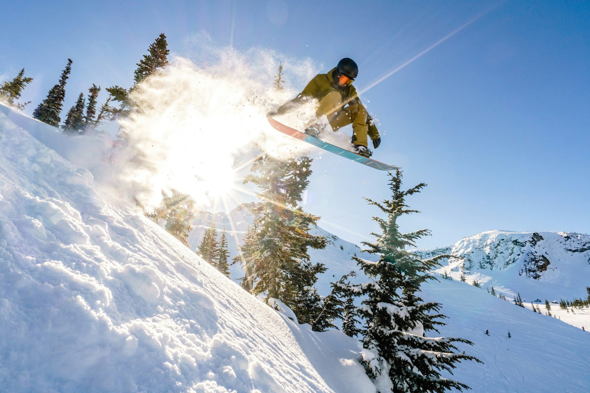 A snowboarder going down a slope among trees on a sunny day