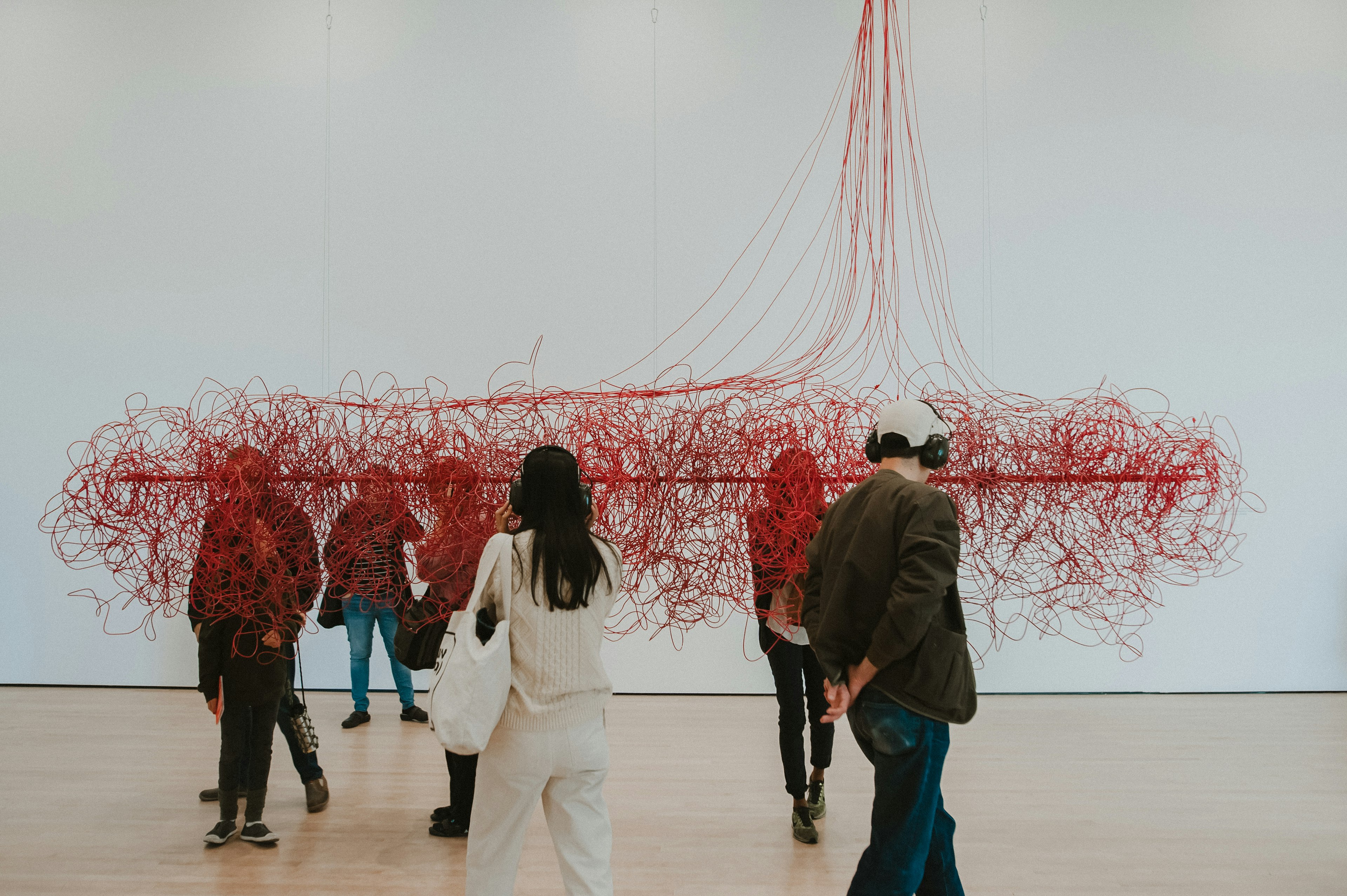 A man and woman admire a sculpture made of red thread in a white room at SF Moma