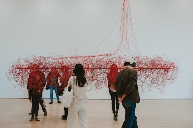 A man and woman admire a sculpture made of red thread in a white room at SF Moma