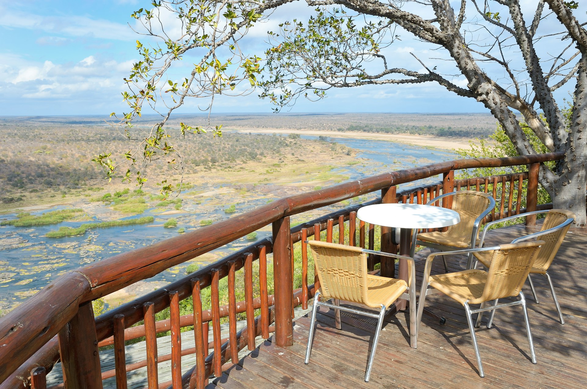 A raised wooden deck with a table and two chairs looking down towards a river in the valley below, the perfect wildlife-watching spot