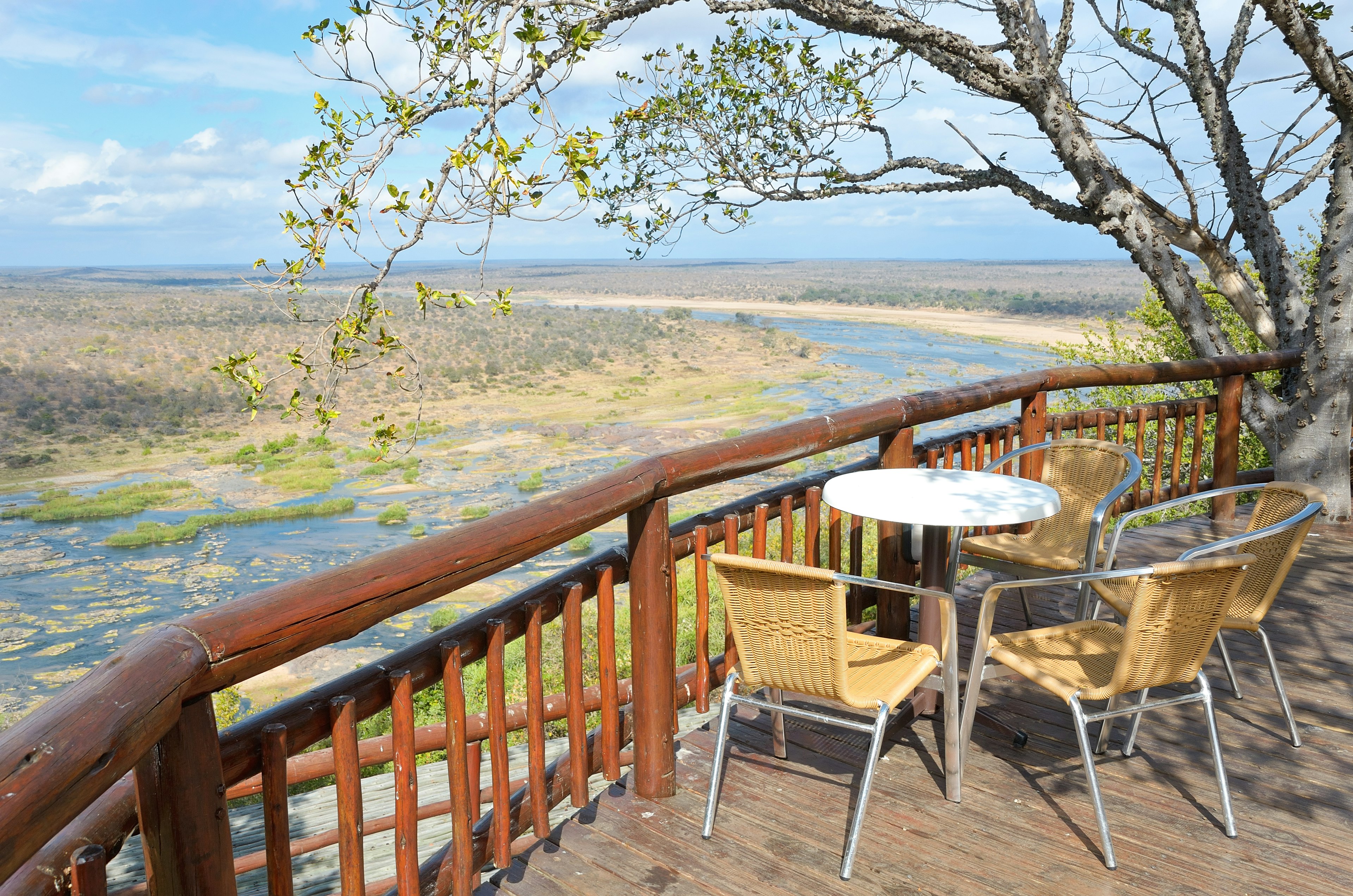 A raised wooden deck with a table and two chairs looking down towards a river in the valley below, the perfect wildlife-watching spot