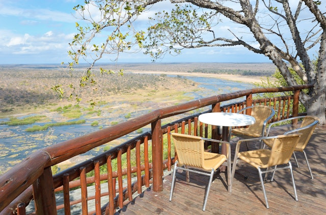 A raised wooden deck with a table and two chairs looking down towards a river in the valley below, the perfect wildlife-watching spot