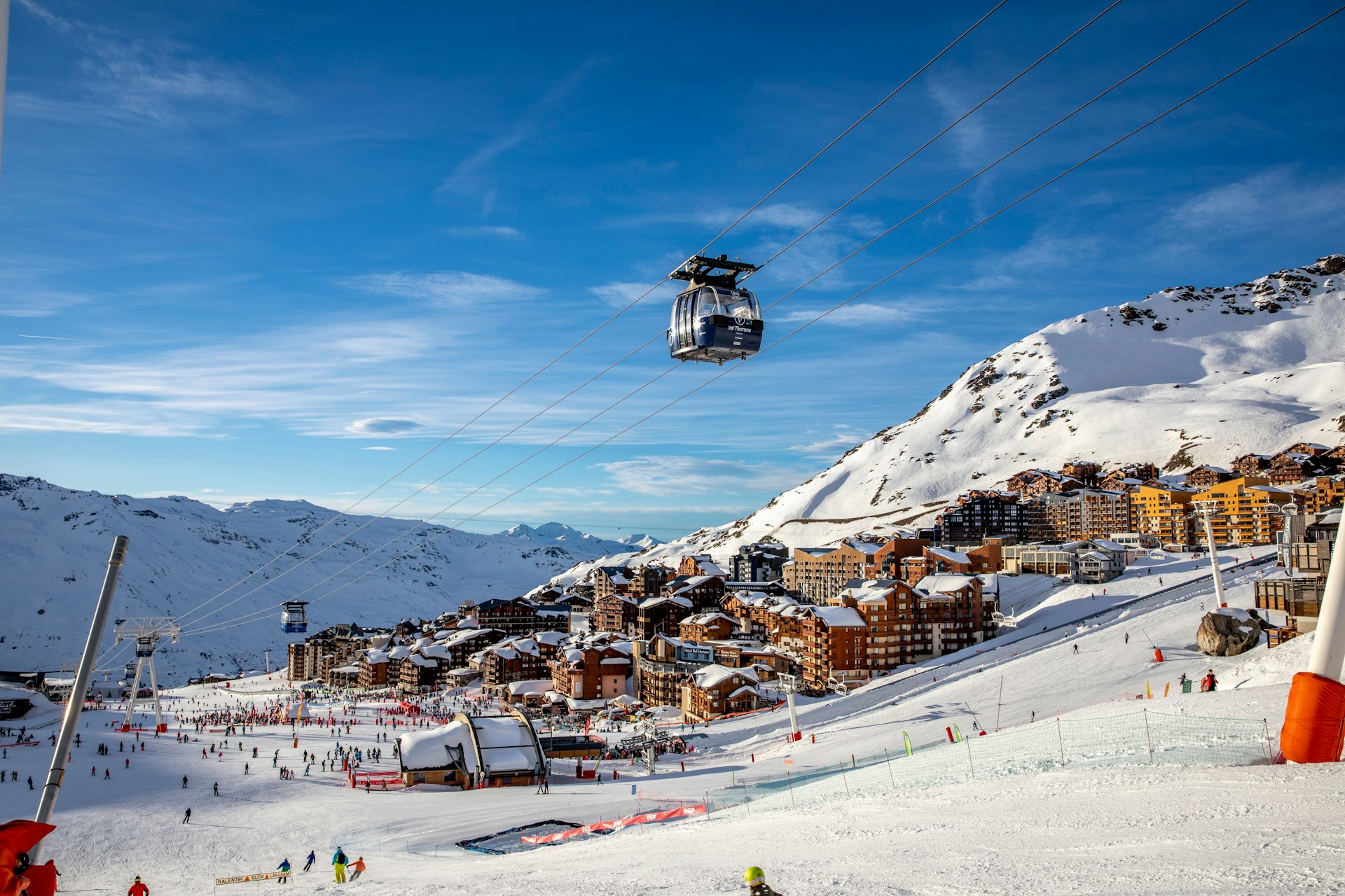 A cable car sails over a ski and snowboard resort with people on the slopes below