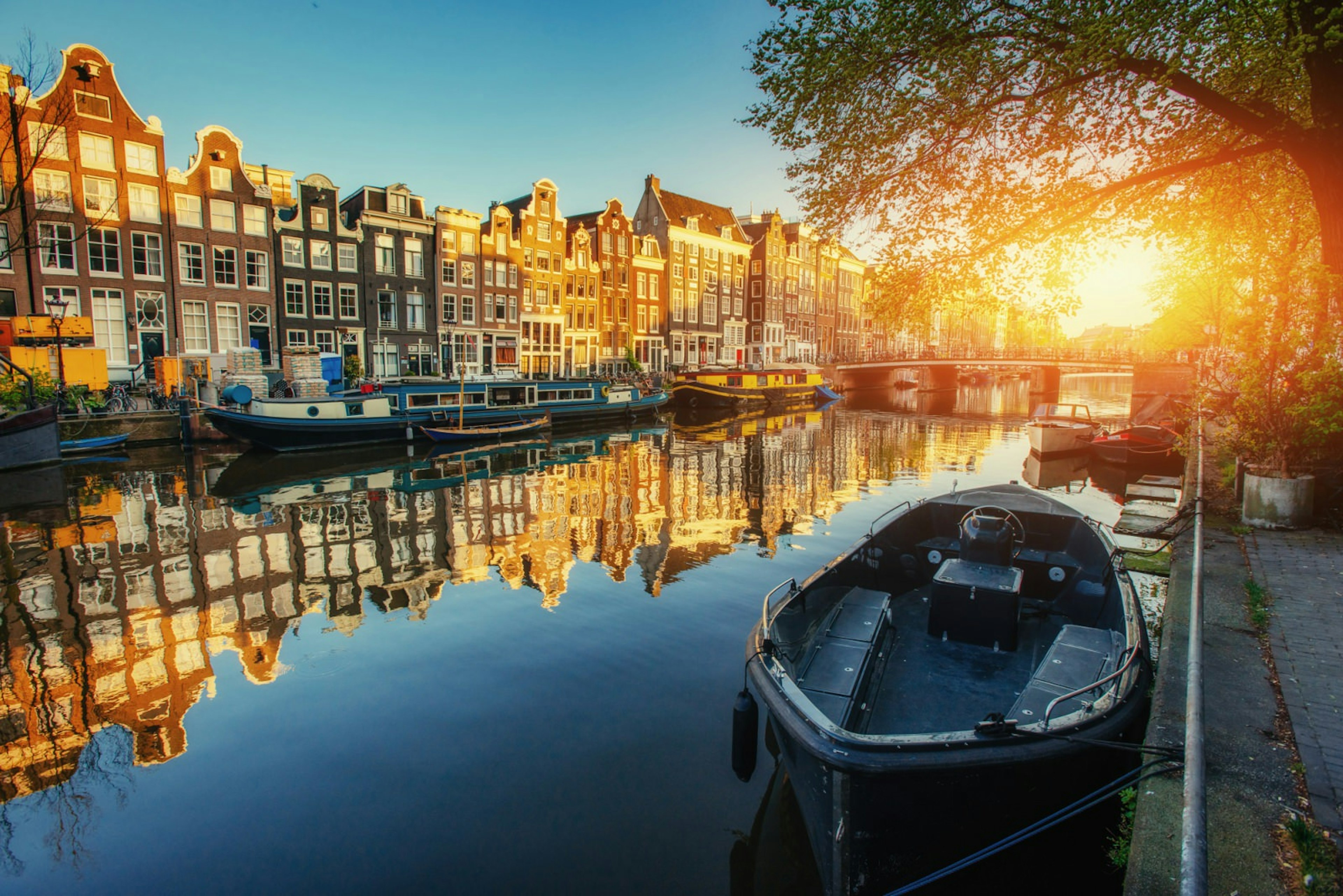 The sun rises over Amsterdam's famed canals with old buildings in the background and an empty boat in the foreground