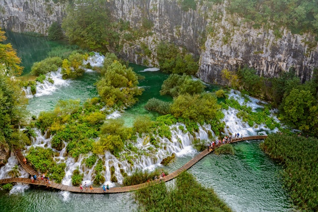 Tourists walk along wooden walkways around waterfalls in a national park