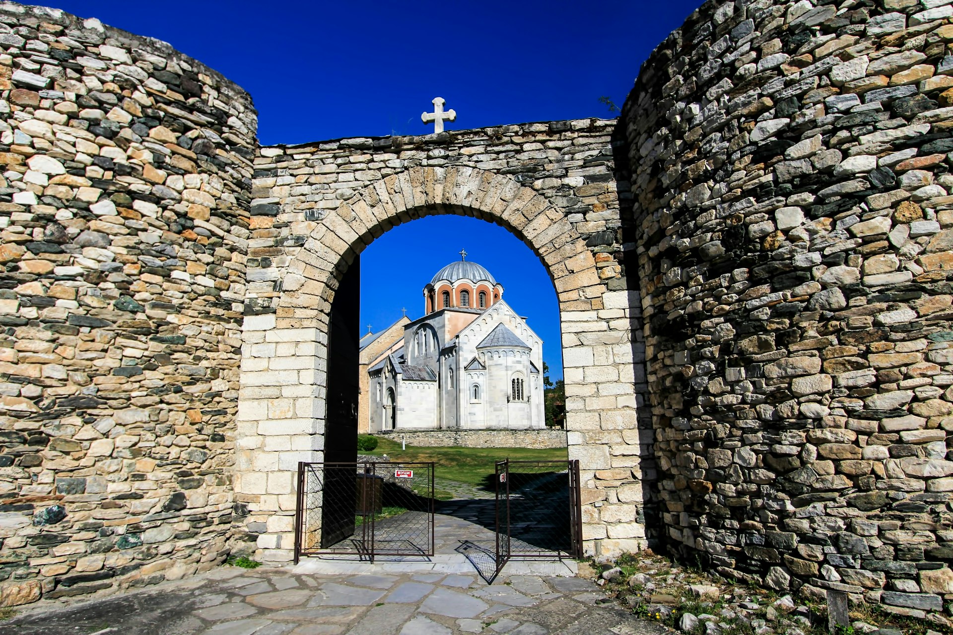 A domed monastery viewed through a stone archway with a cross on top