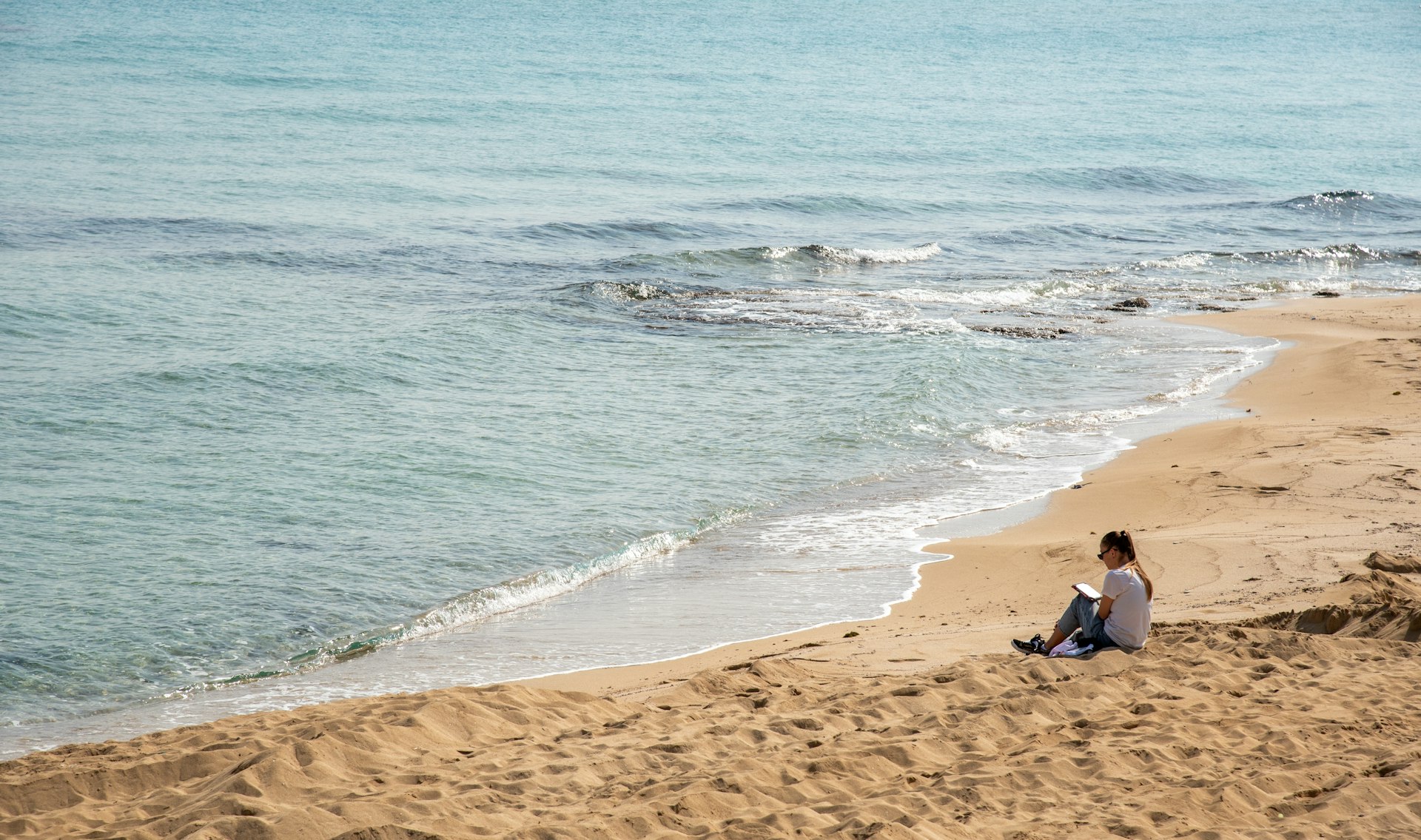 A woman reads a book on the sandy beach in winter in Protaras, Cyprus